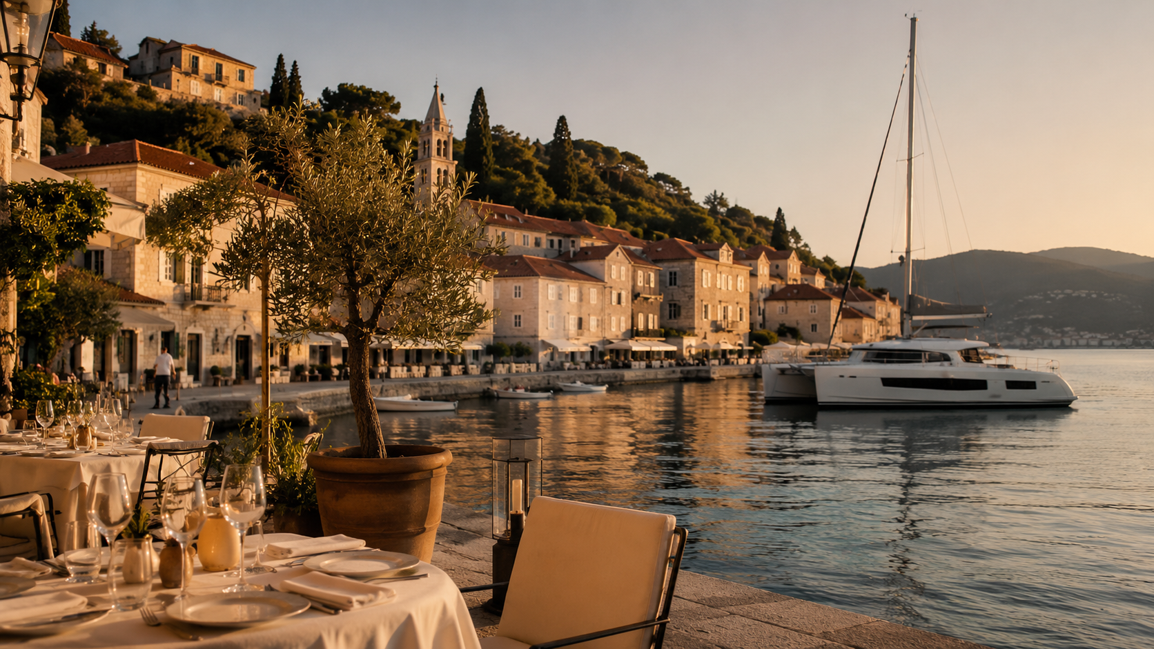 Elegant Mediterranean waterfront restaurant terrace with calm harbour water and a catamaran nearby
