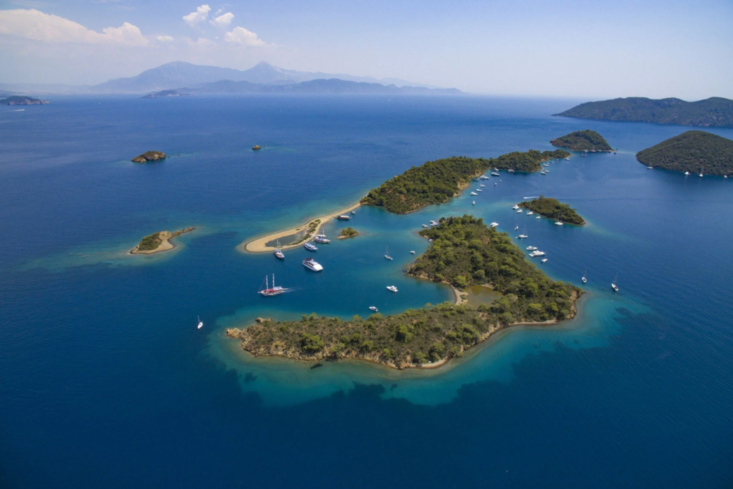 A group of small islands with sandy beaches and green vegetation surrounded by blue water, with boats anchored around.