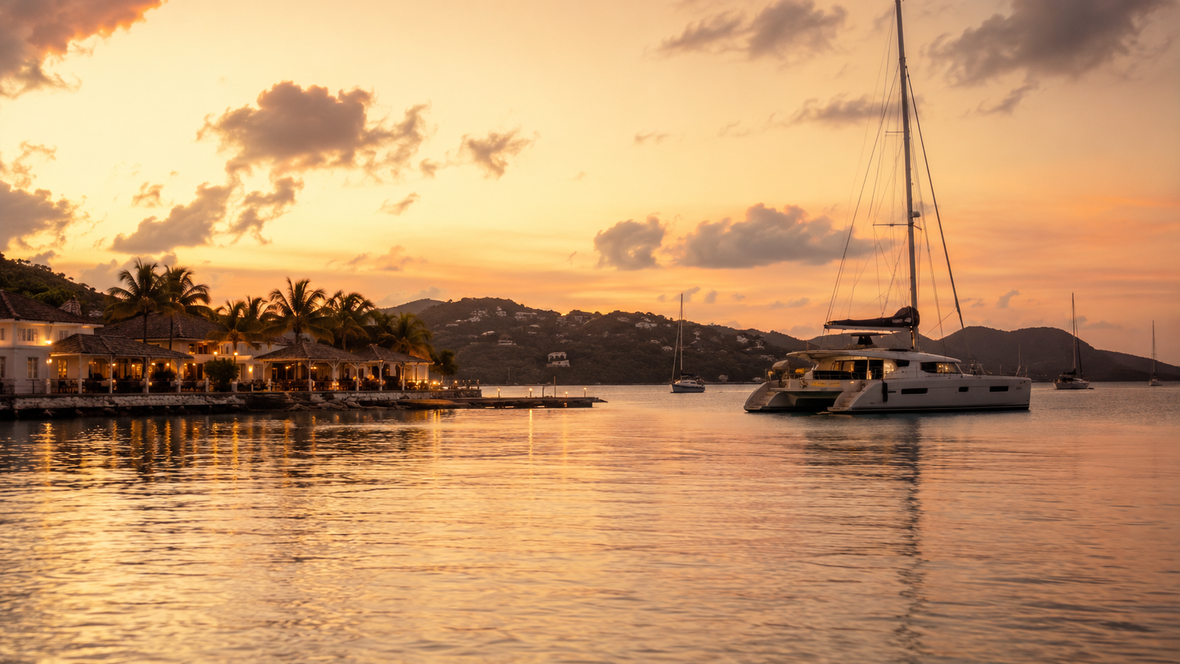 Modern catamaran at anchor near a peaceful Caribbean harbour with softly lit waterfront restaurants at sunset