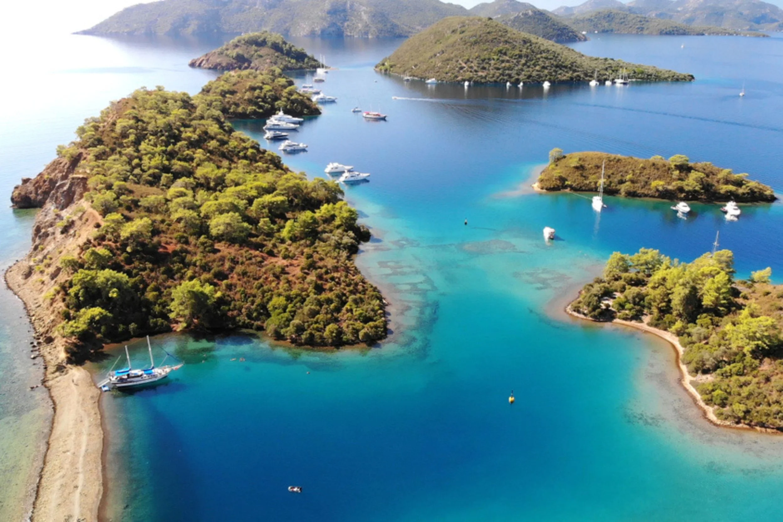 Aerial view of a coastal area with small islands covered in greenery, surrounded by clear blue water with boats anchored nearby.