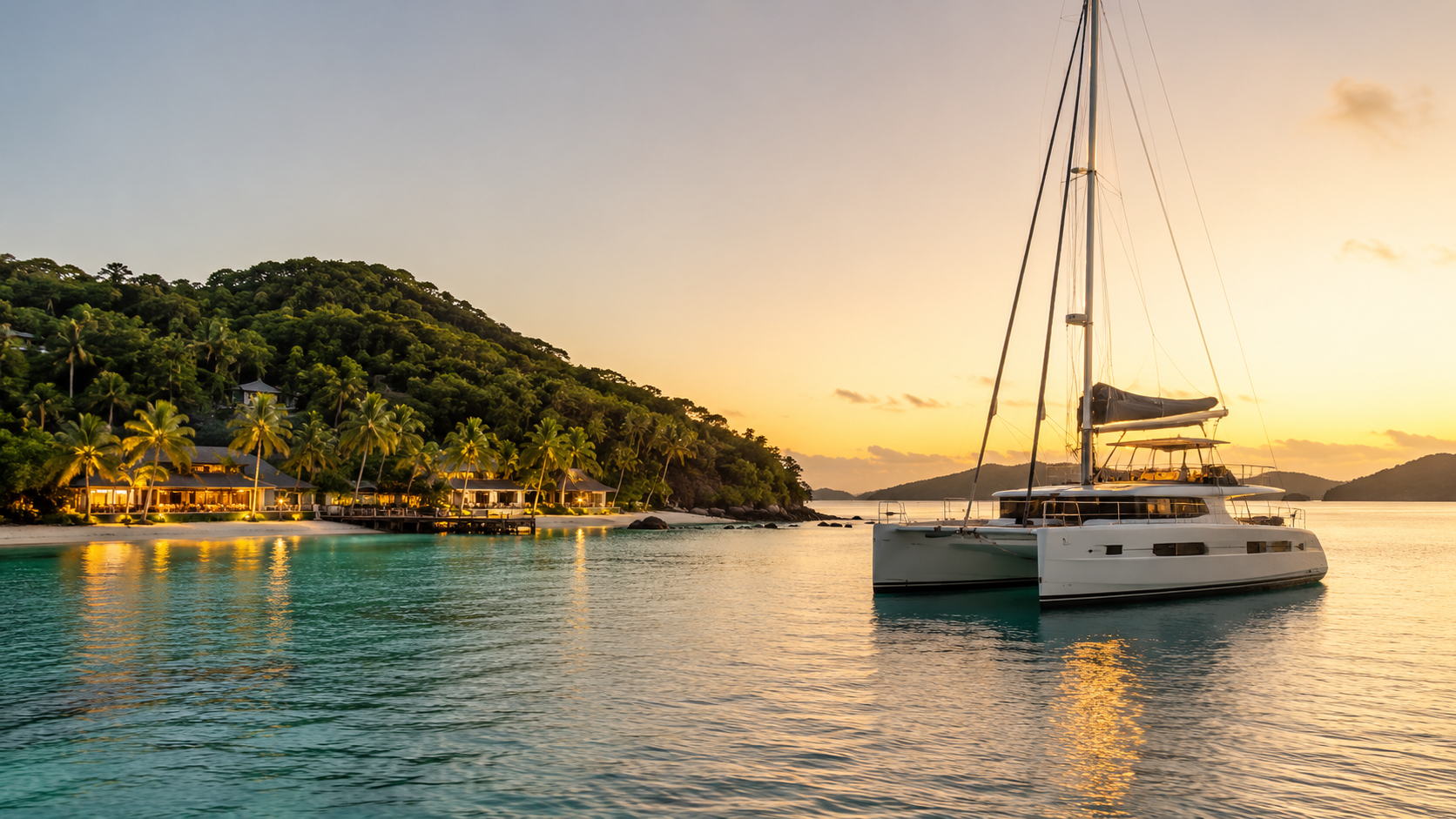 Modern catamaran at anchor in a peaceful Caribbean bay at sunset, with turquoise water and soft lights along an island shoreline.