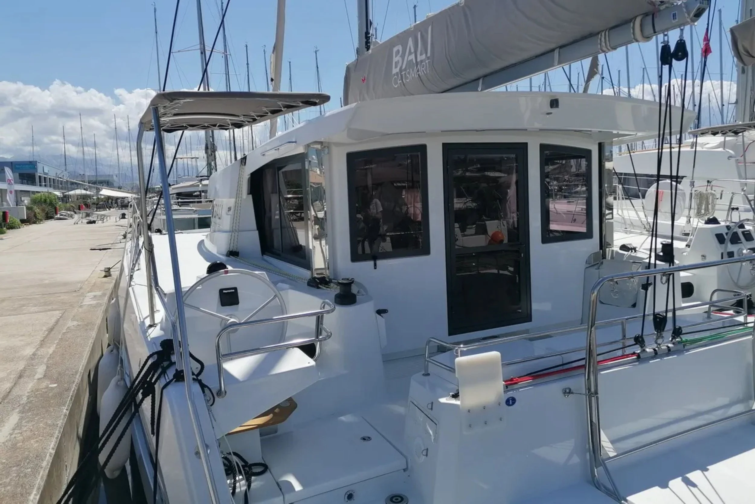 A white yacht docked at a marina with other boats in the background, under partly cloudy skies.