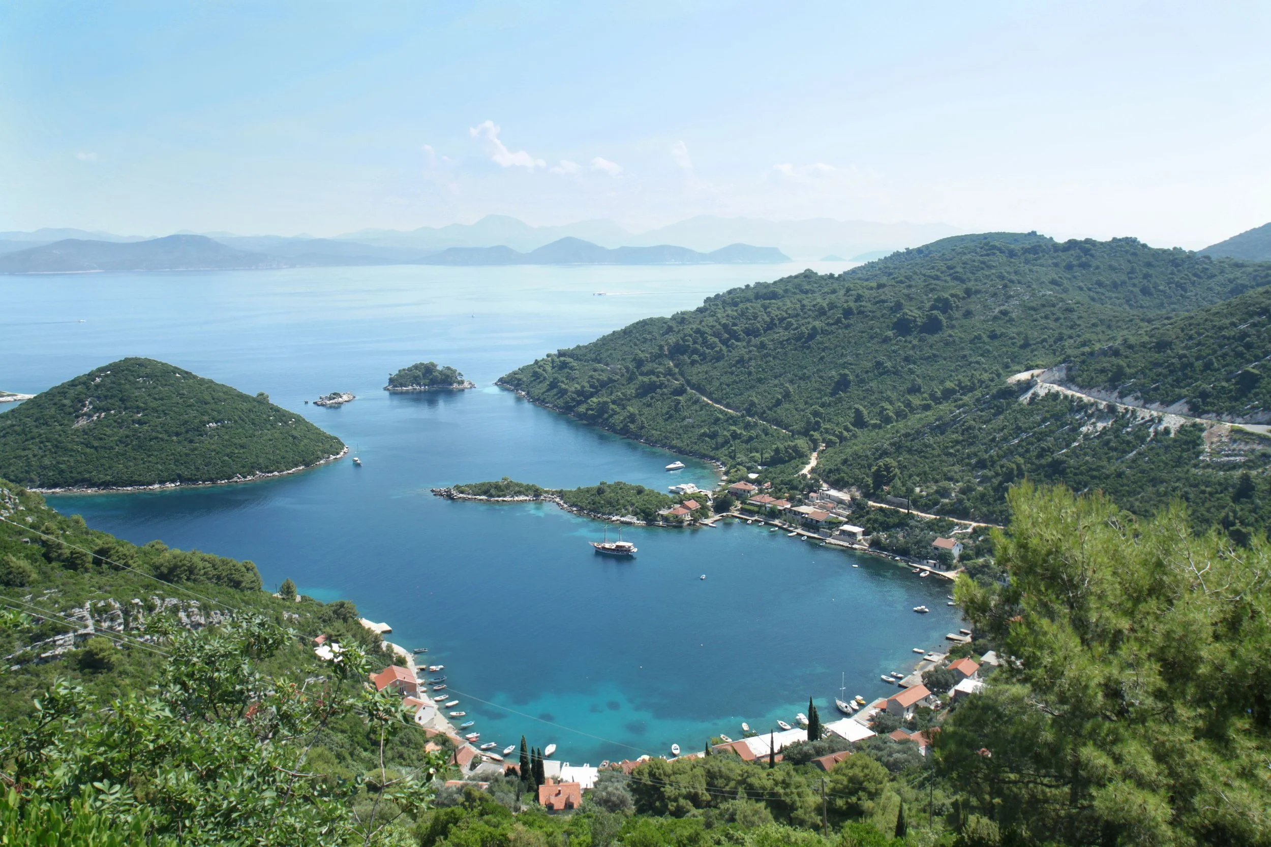 Scenic view of a coastal bay with surrounding green hills, small islands, and boats, overlooking the open sea.