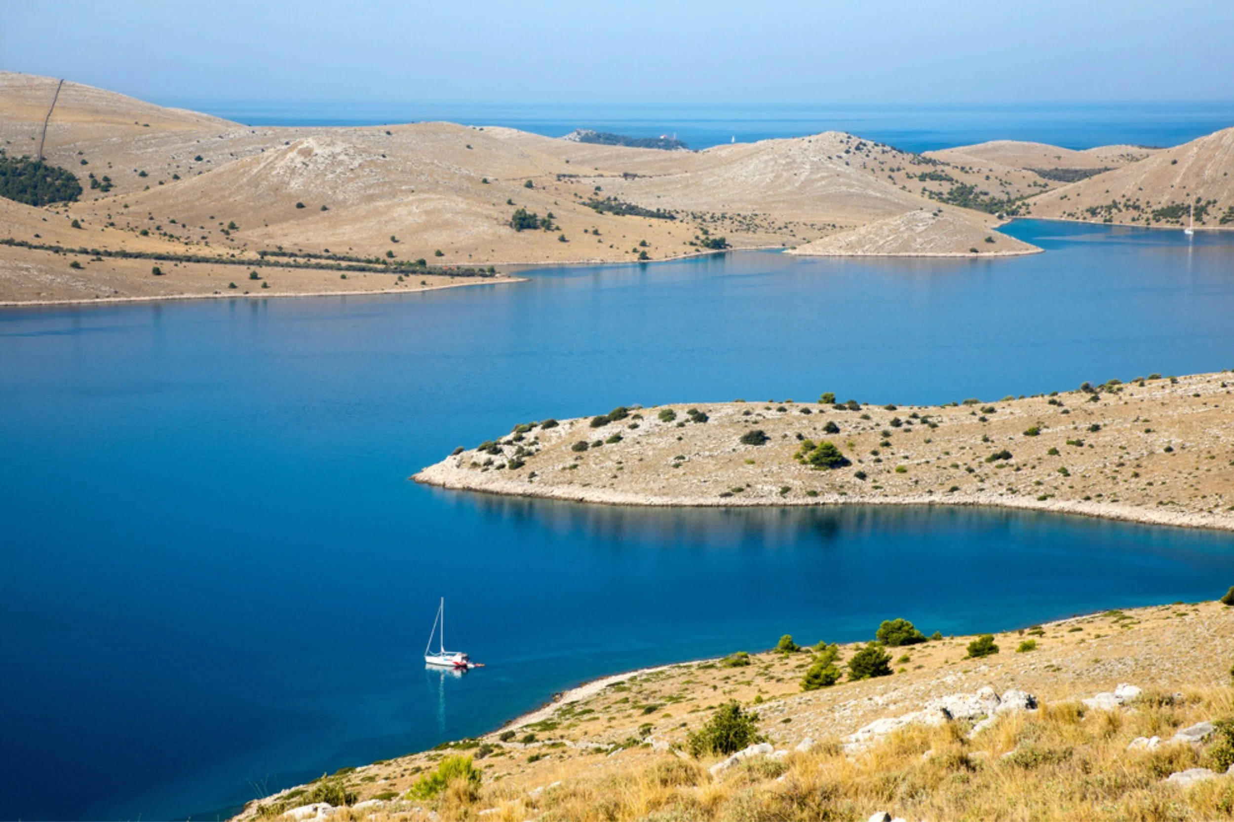 A boat sailing in a large body of water surrounded by arid, hilly landscape with sparse vegetation.