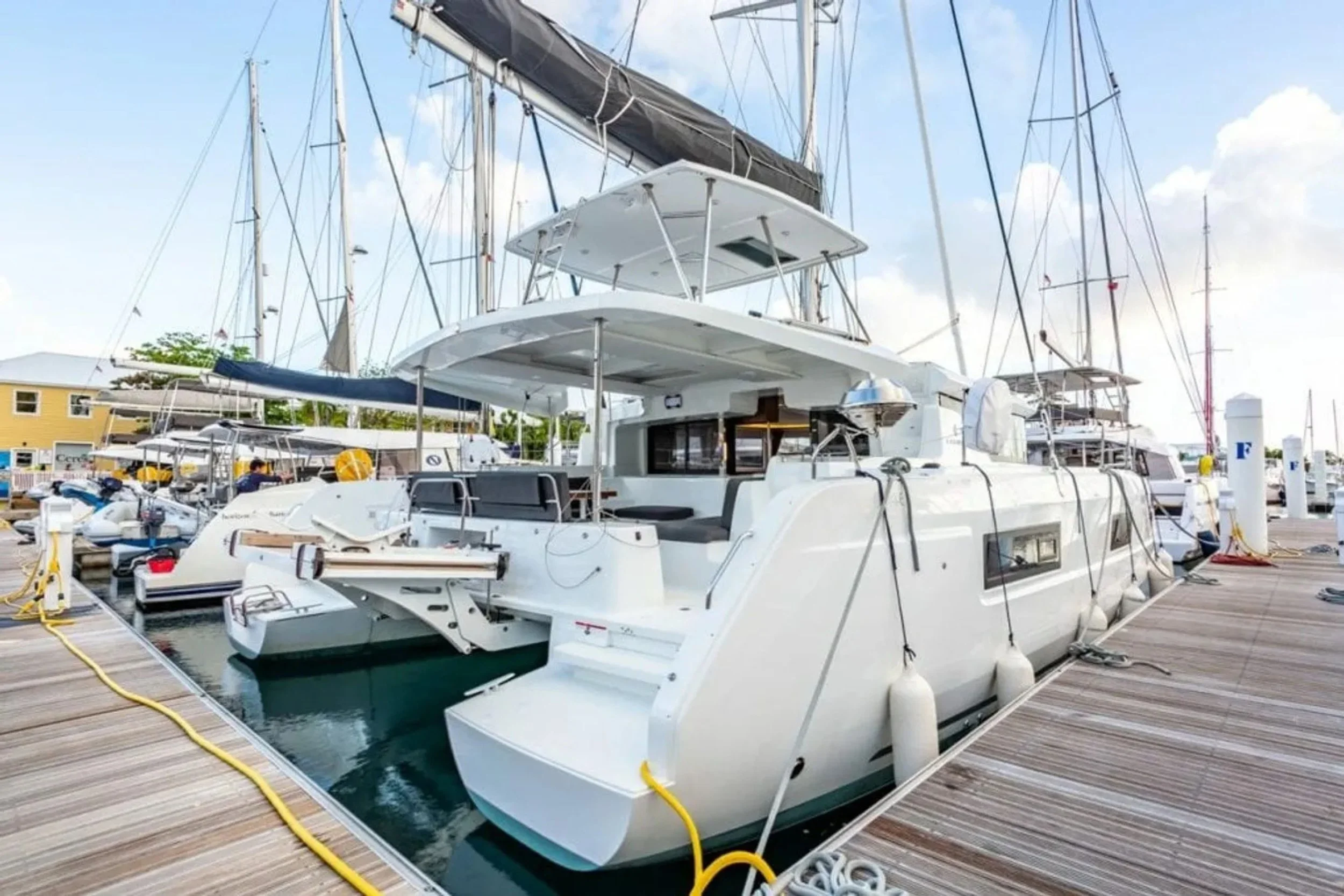 A white luxury yacht is docked at a marina with other boats, with buildings and a sky with light clouds in the background.