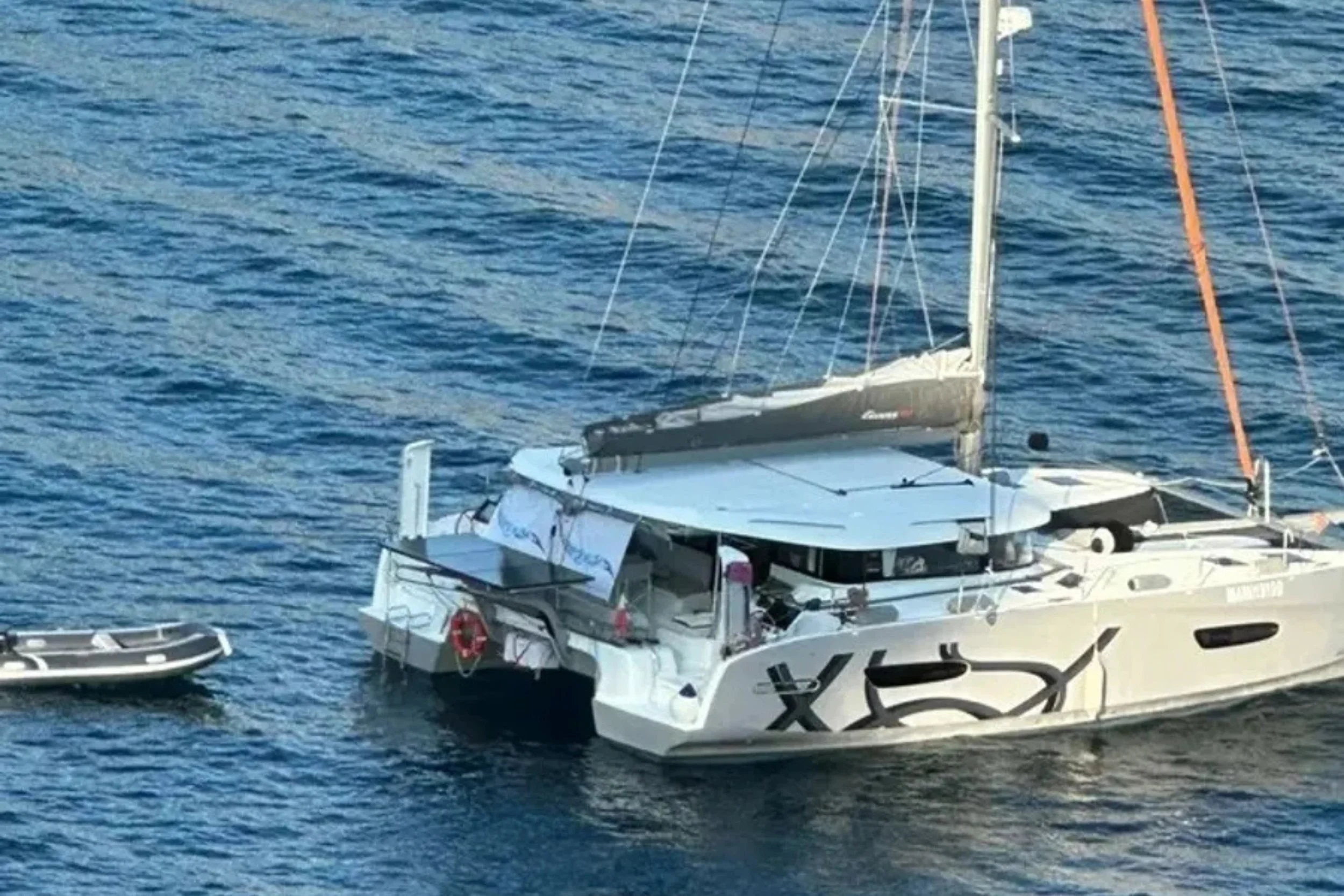 A white yacht with a small inflatable boat attached, sailing on blue water.