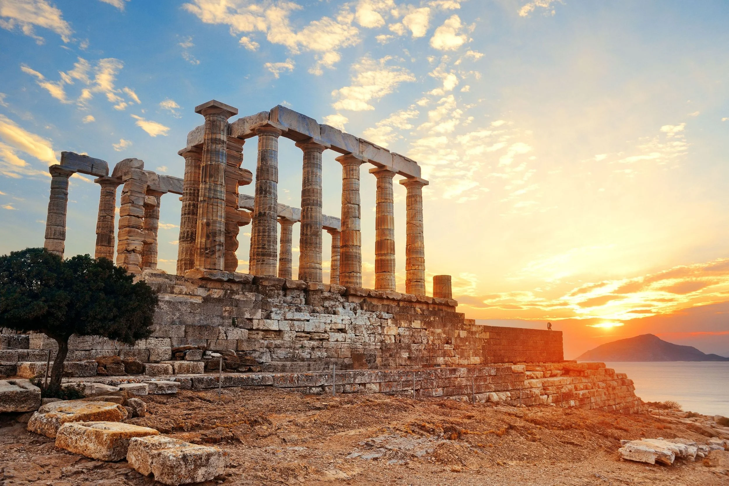 Ancient Greek ruins with tall stone columns at sunset over the ocean and a distant island.