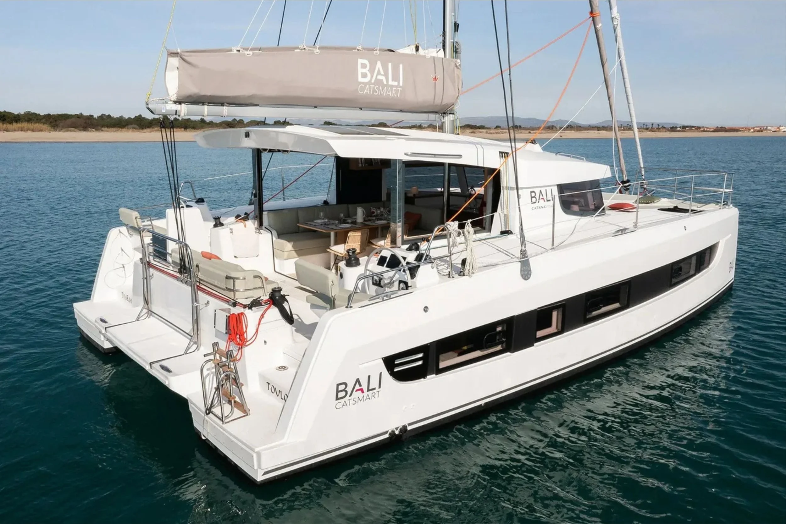 Modern white sailing yacht named Bali Cat Smart on calm water with a coastal landscape in the background