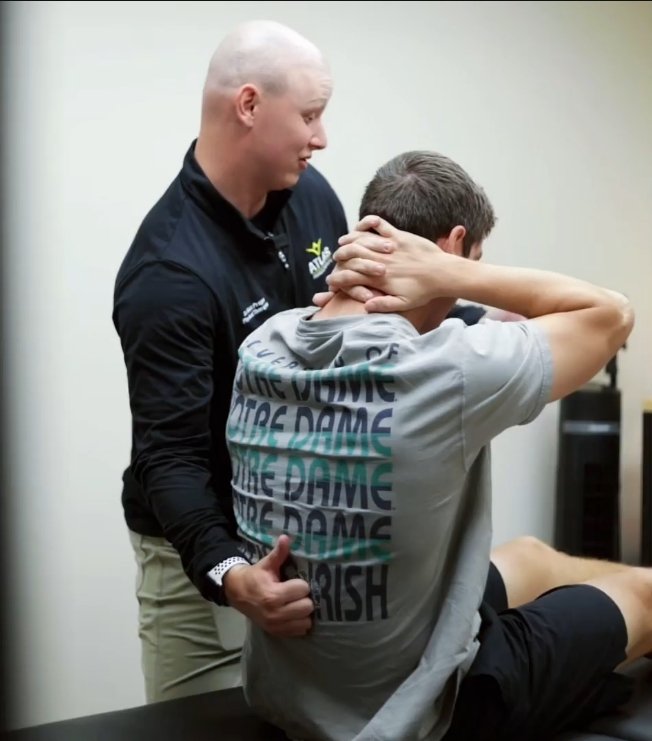 A healthcare professional, possibly a physical therapist or chiropractor, is performing a neck stretch or assessment in Atlas physical therapy office in Huntington, NY. The professional is standing behind the patient, guiding the movement.