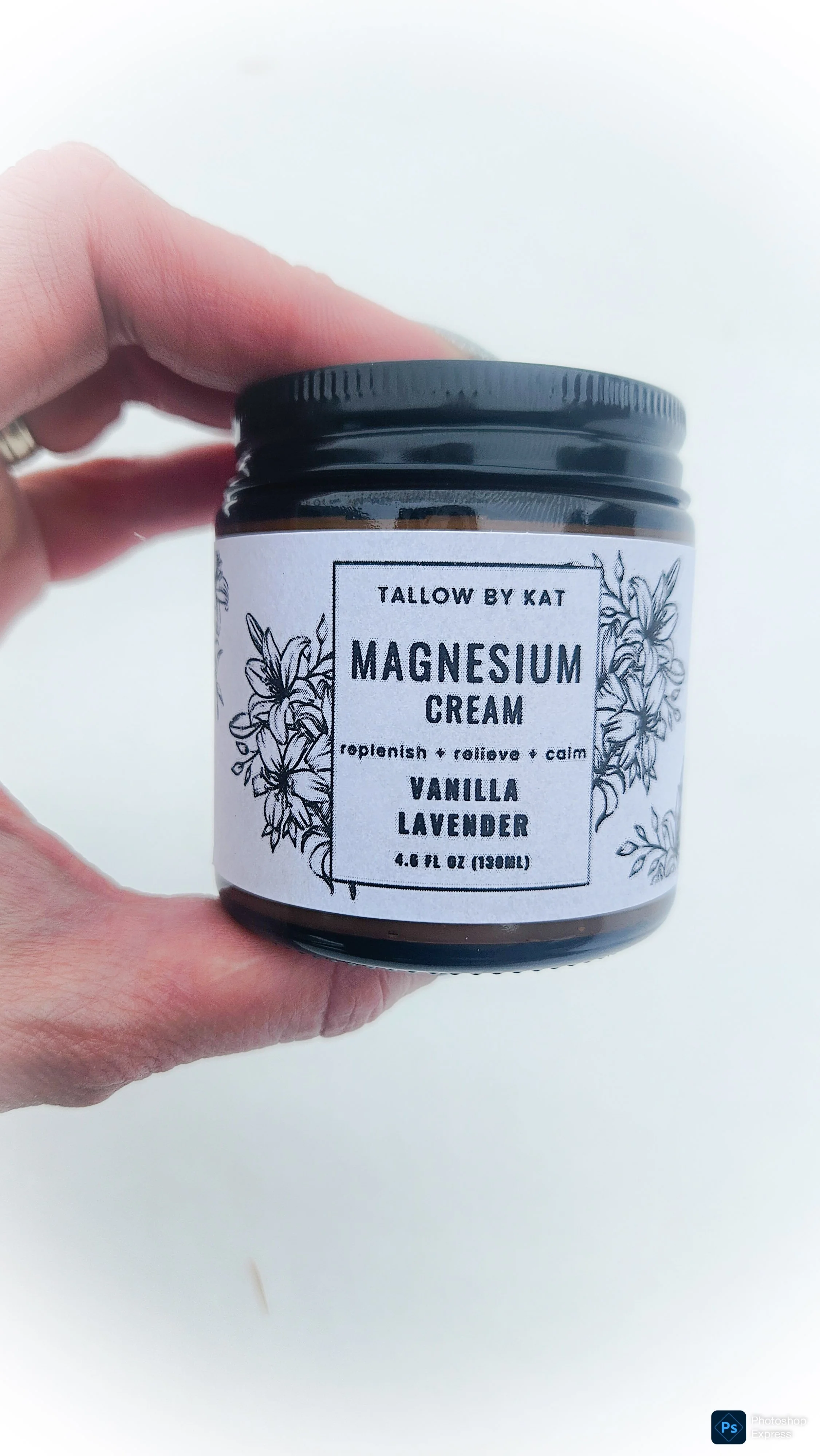 A hand holding a jar of magnesium cream labeled with floral illustrations, with ingredients vanilla and lavender, and the description to relax and calm.