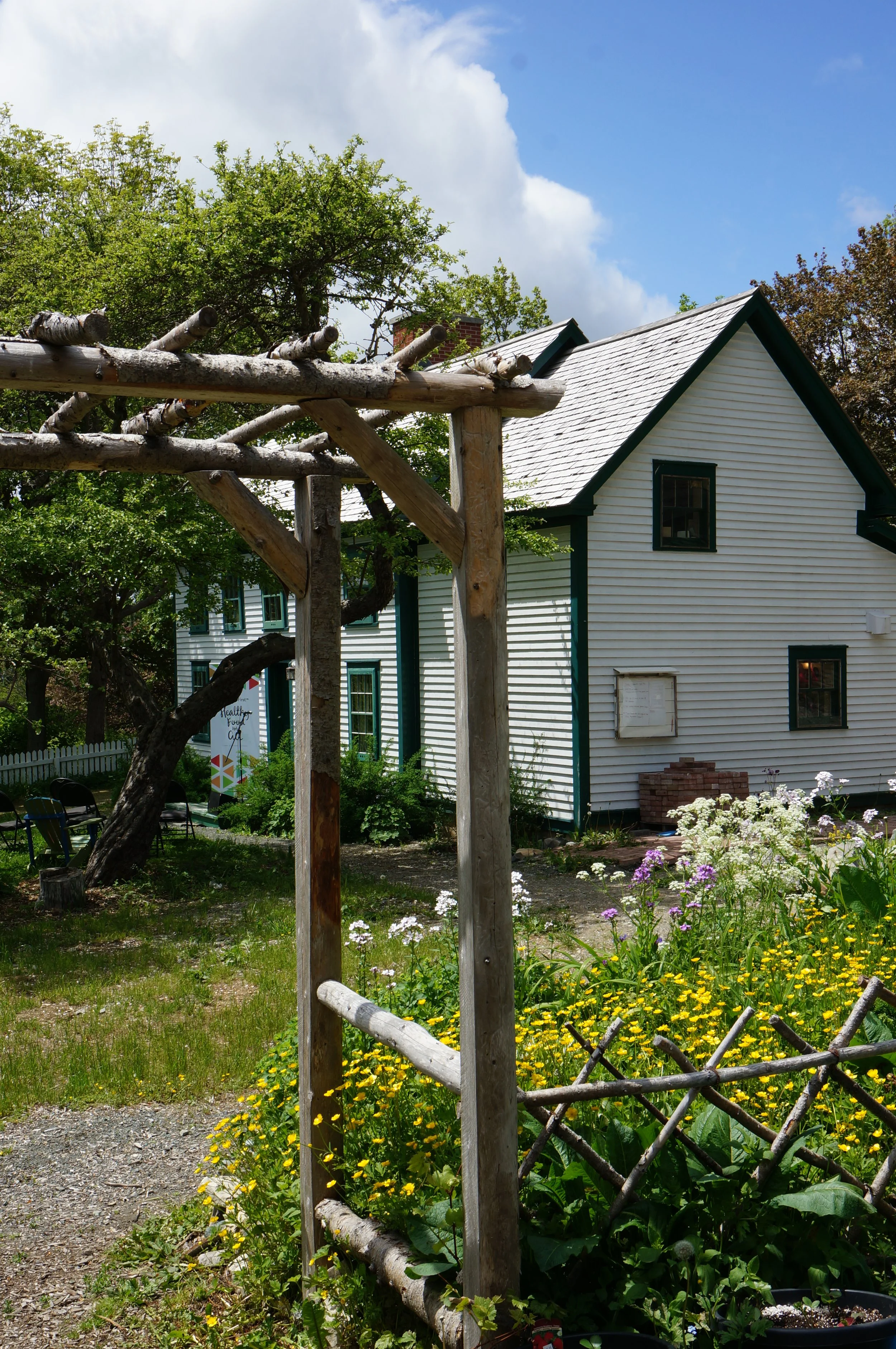 A rustic wooden archway in front of Thimble Cottage, with the surrounding gardens in full bloom.