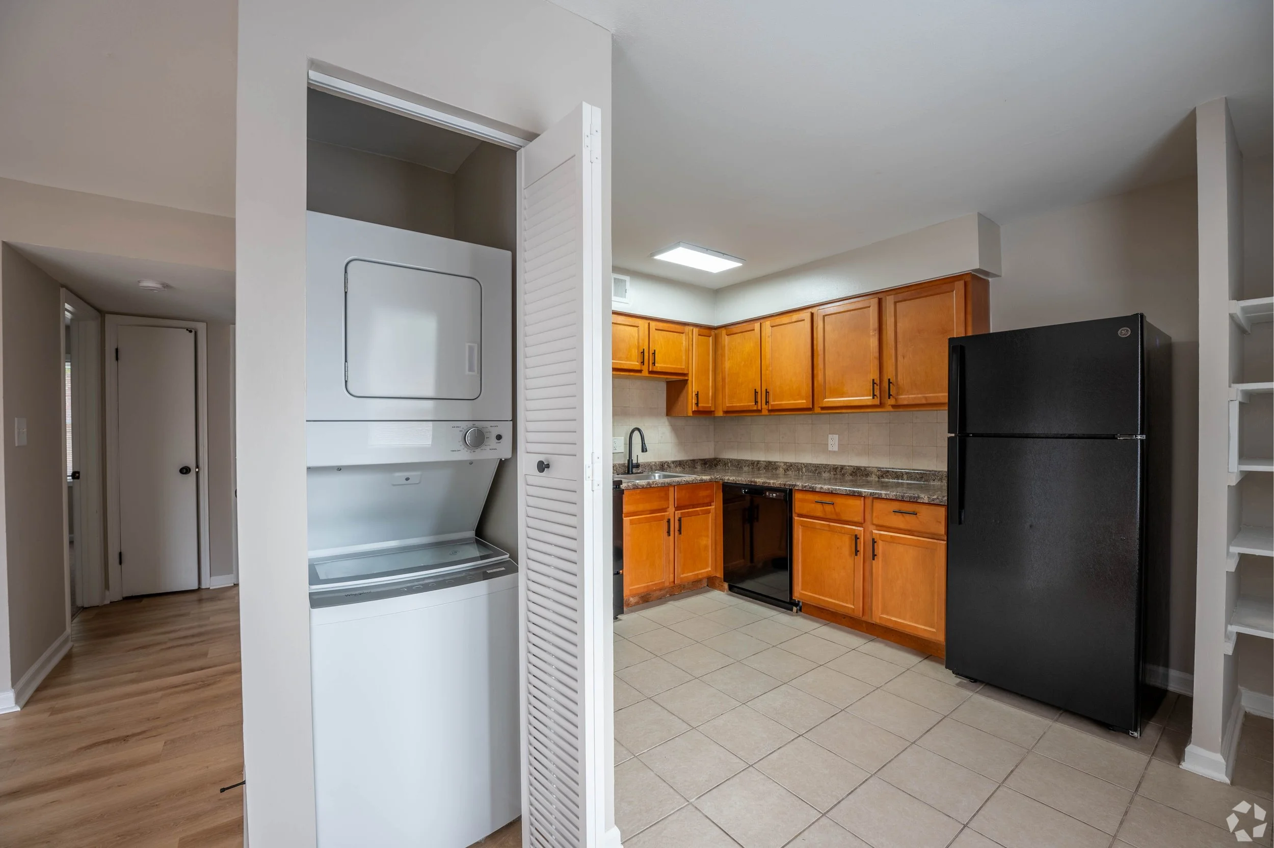 Kitchen with wooden cabinets, black refrigerator, and laundry area with stacked washer and dryer