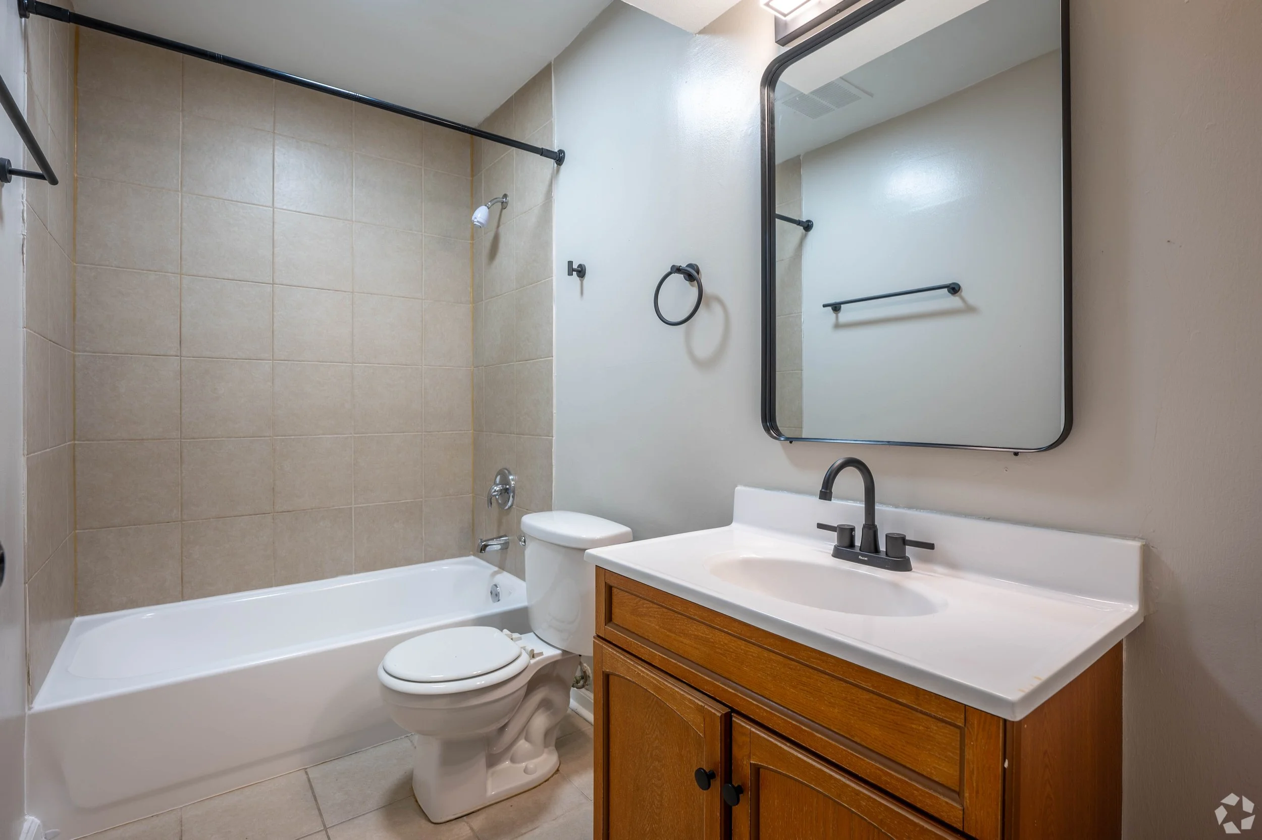 Bathroom with bathtub, toilet, and wooden vanity with sink, mirror, and towel rack.