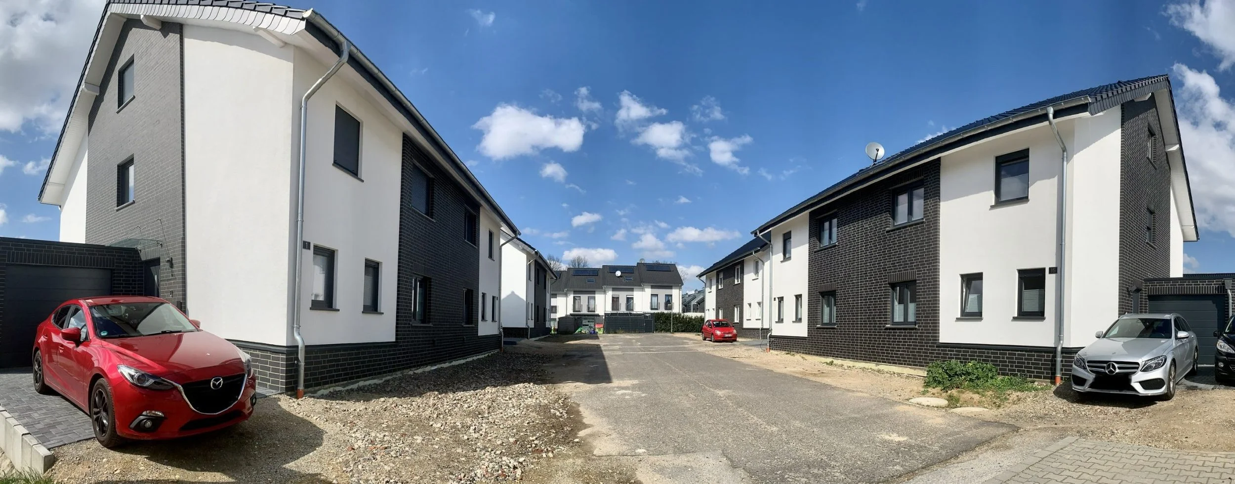Modern residential buildings with black and white facades, parked cars, and a clear blue sky.