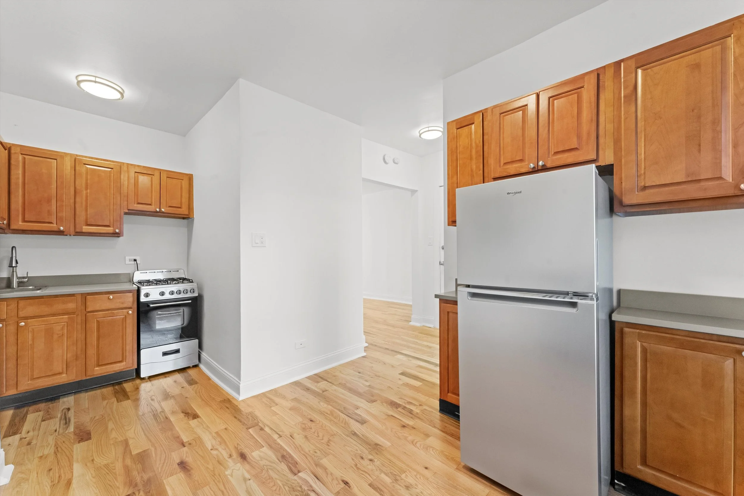 Kitchen with wooden cabinets, a silver refrigerator, a small stove, a sink, and hardwood floors.