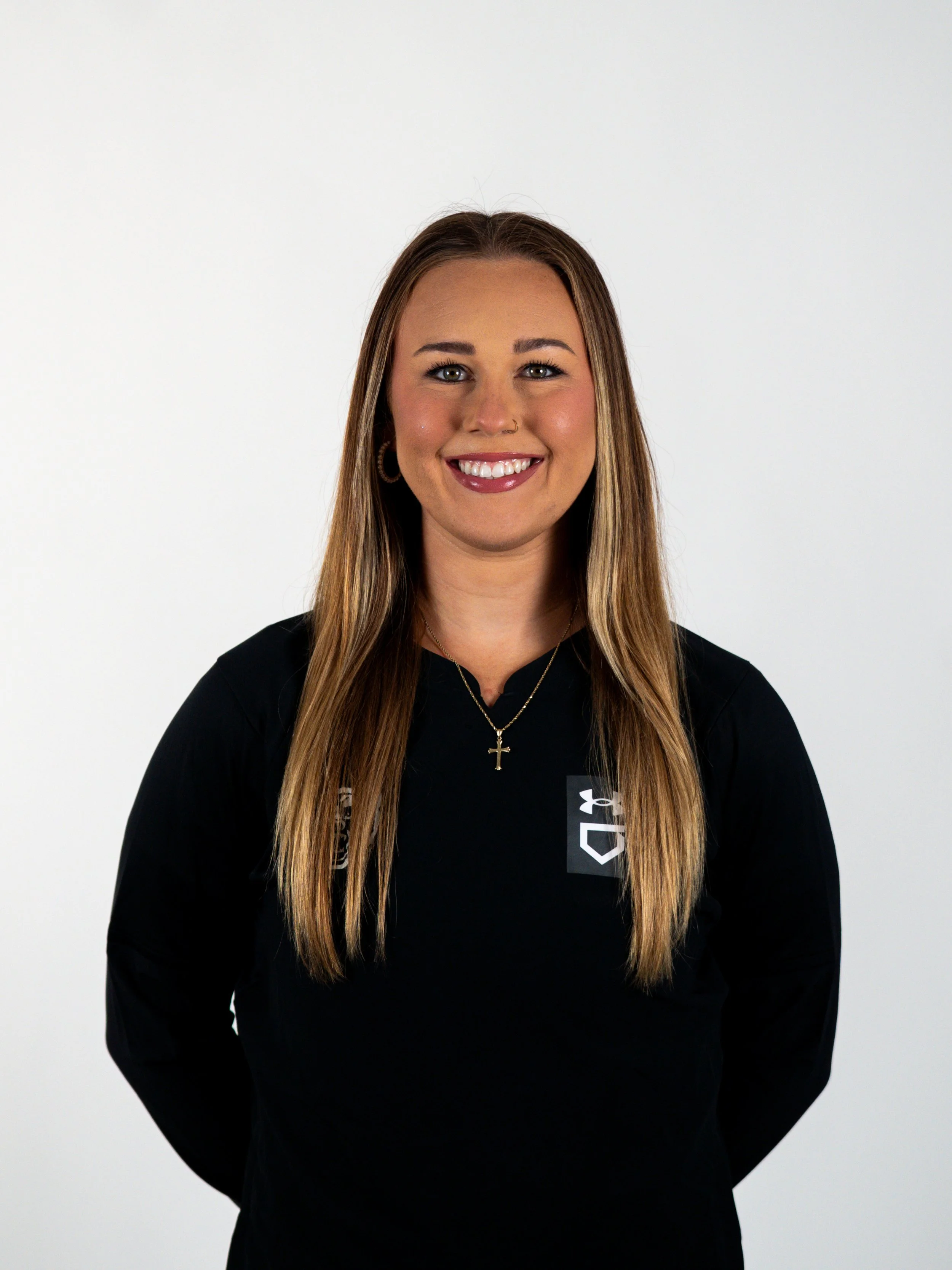 A woman with long braided hair wearing a blue 'Bluebonnets' t-shirt, smiling outdoors on a sunny day.