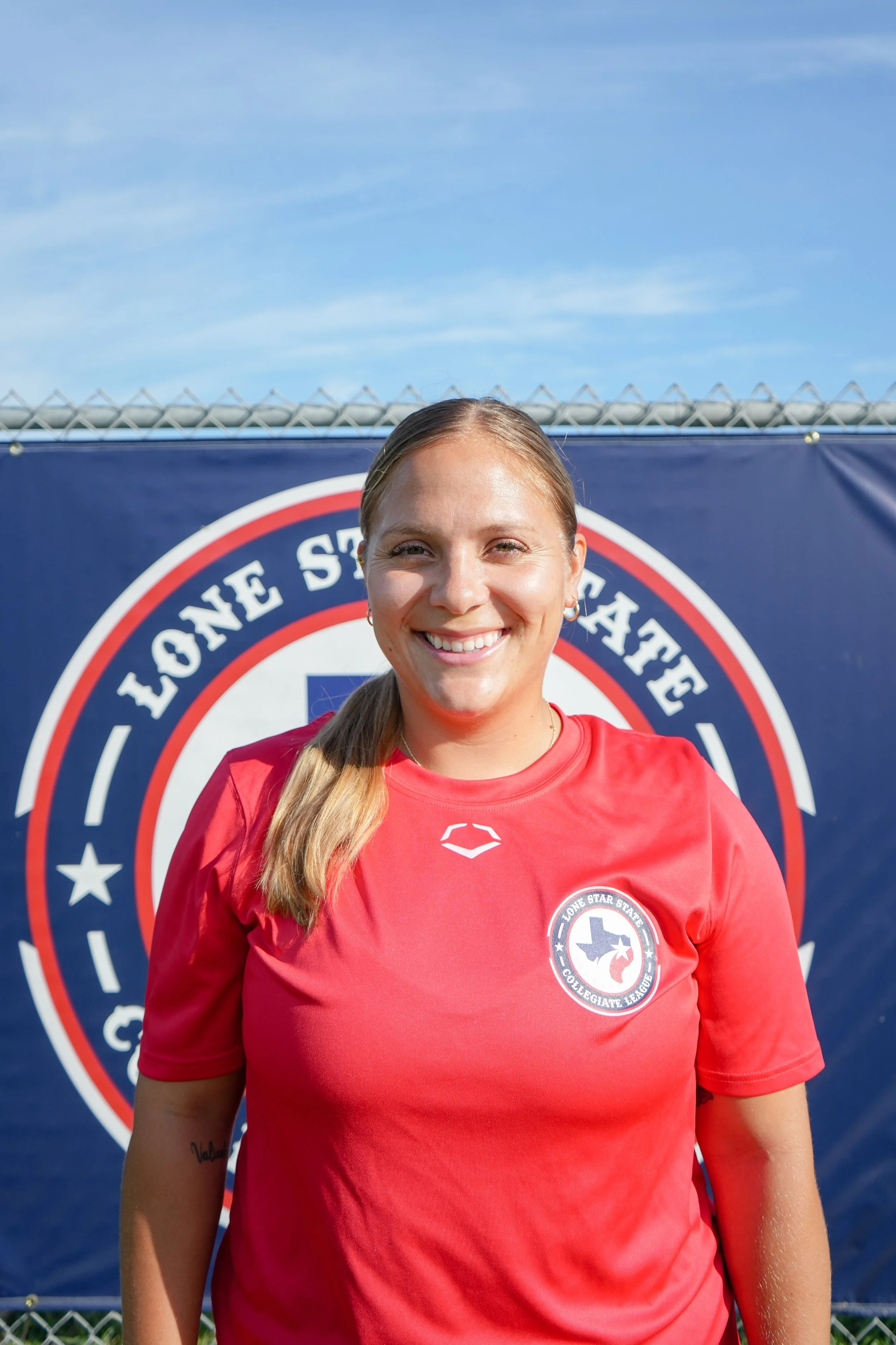 smiling young woman in a red sports shirt standing outdoors in front of a banner that reads 'Lone Star State' with a Texas map and star logo.