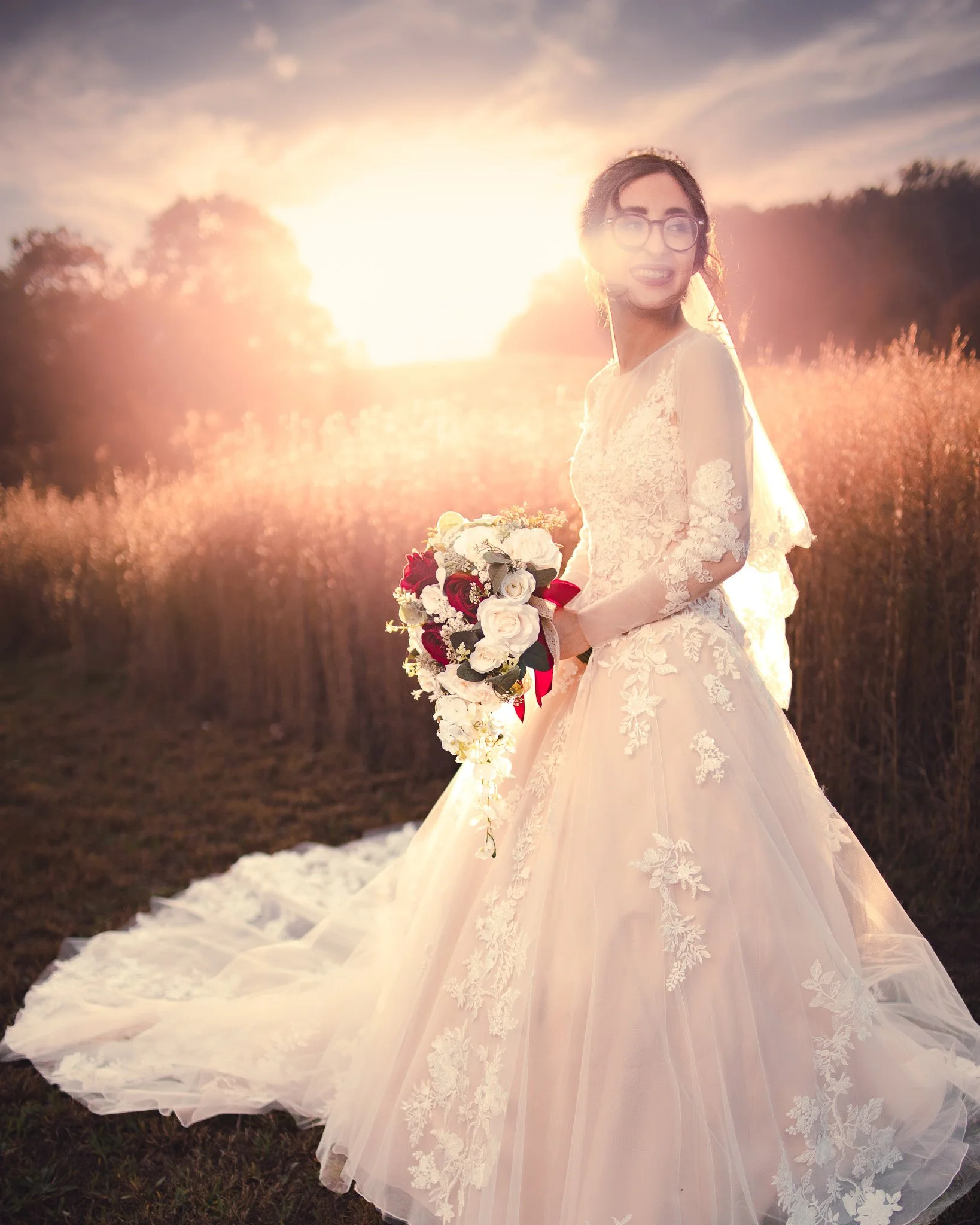 Bride in a lace wedding dress holding a bouquet outdoors during sunset.