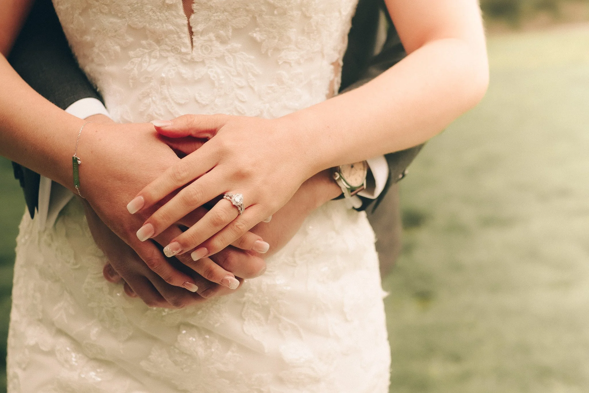 Close-up of a bride and groom holding hands, showing a wedding ring on the bride's finger.