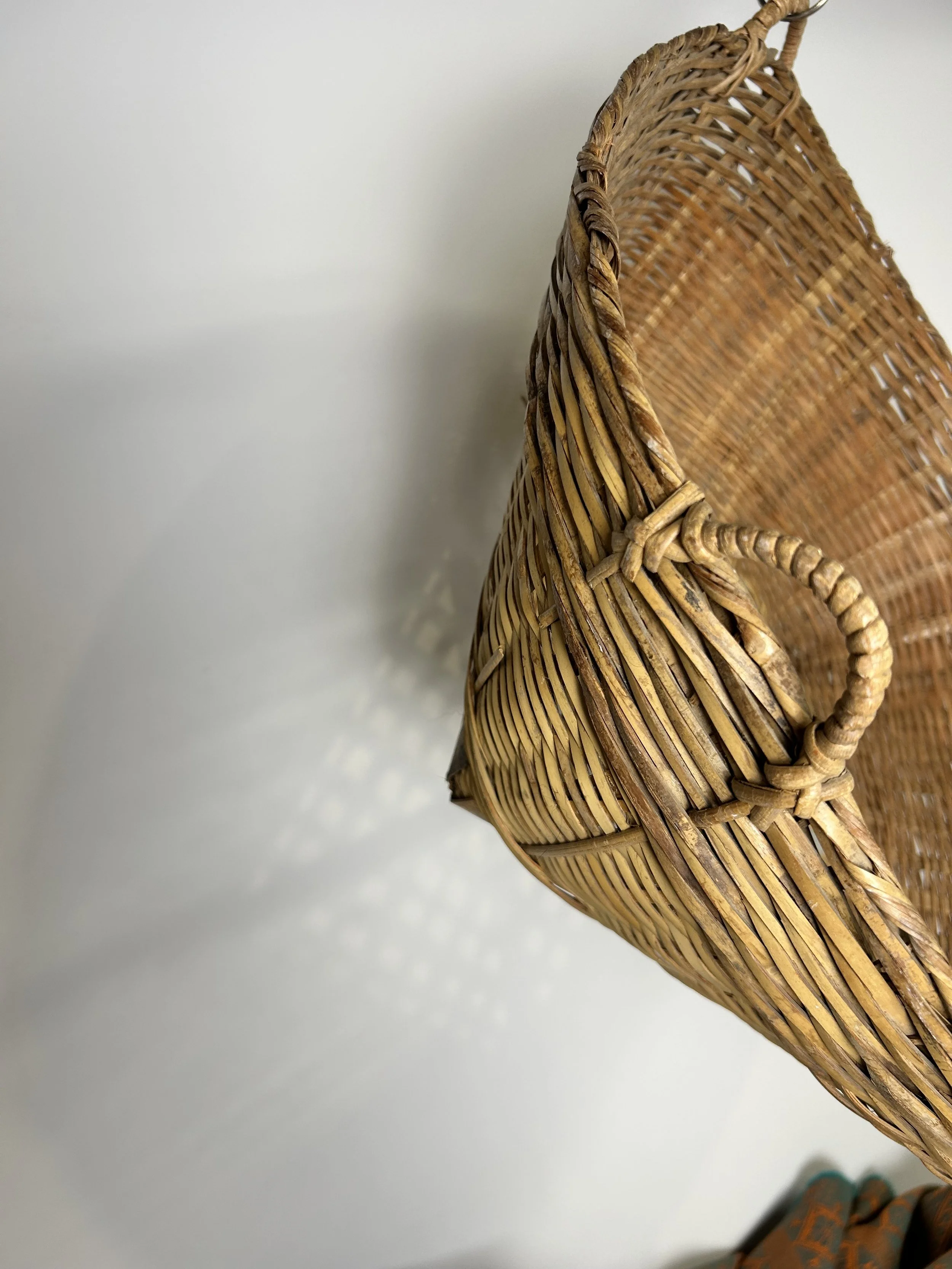 Close-up of a woven wicker basket with a curved handle, casting a shadow on a white surface.