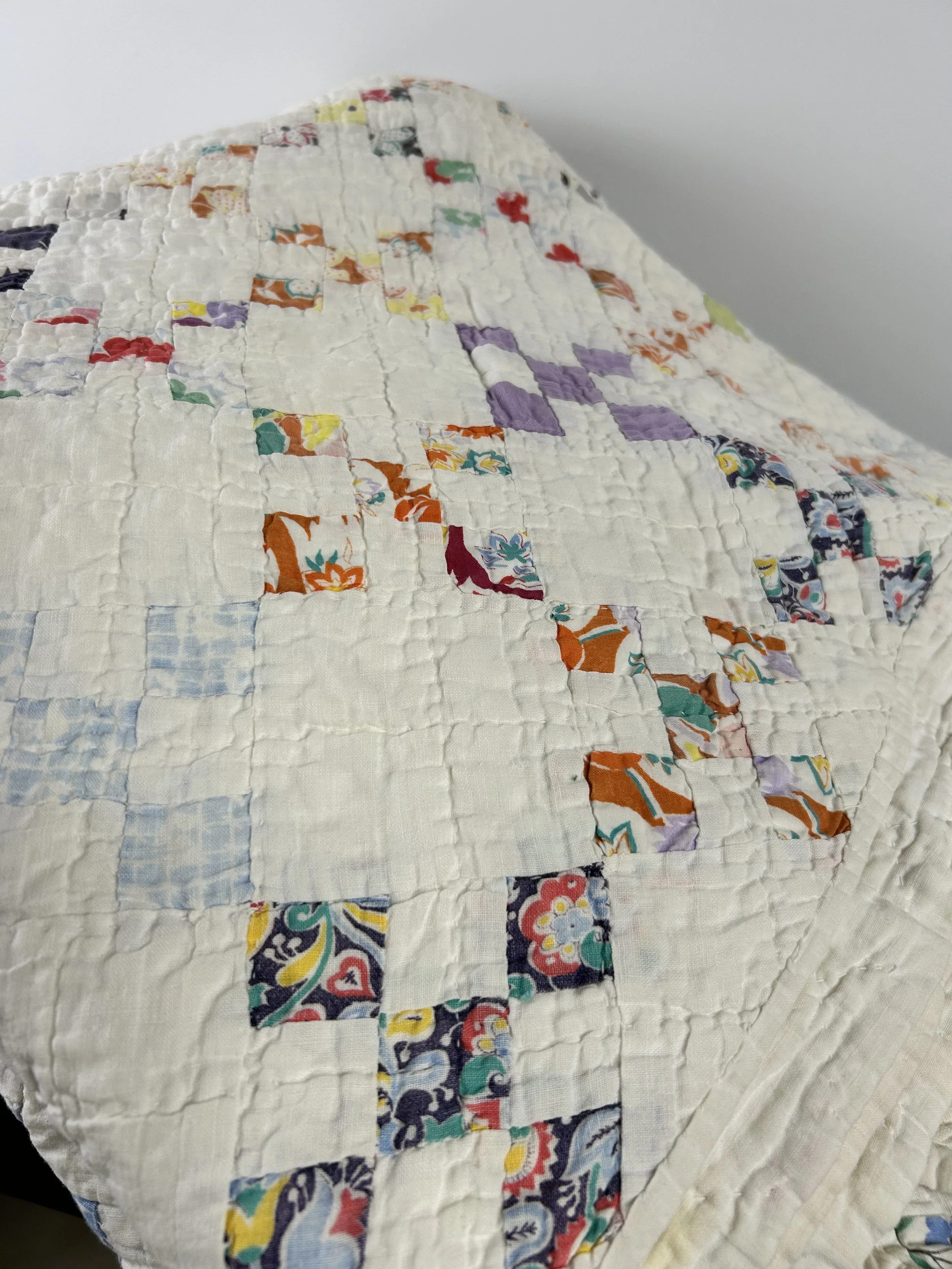 Close-up of a quilted fabric with patchwork design, featuring various colorful and patterned fabric pieces sewn onto a white background.
