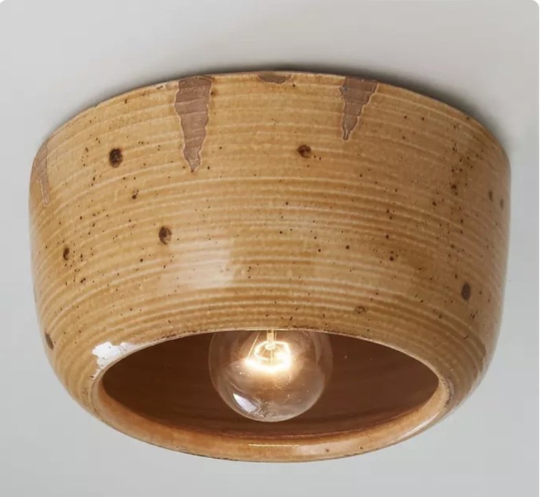 Close-up of a ceiling light fixture with a round, aged ceramic casing surrounding a single exposed light bulb.