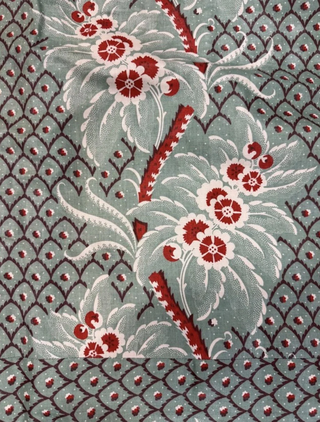 Close-up of a decorative fabric with a floral design in red, white, and green, featuring detailed flowers and leaves on a patterned background.