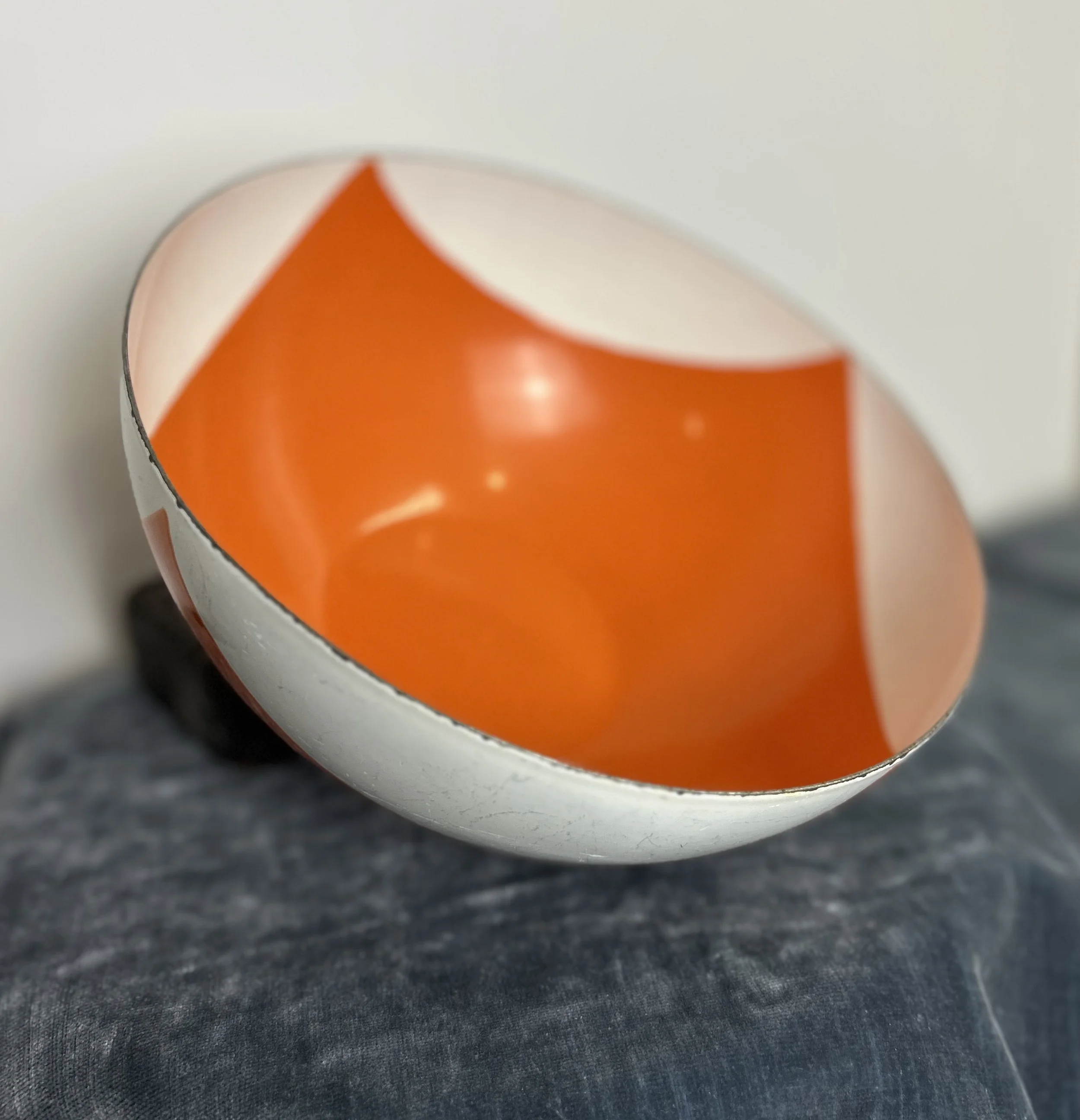 A broken white and orange sphere with a reflective interior, resting on a dark fabric surface.