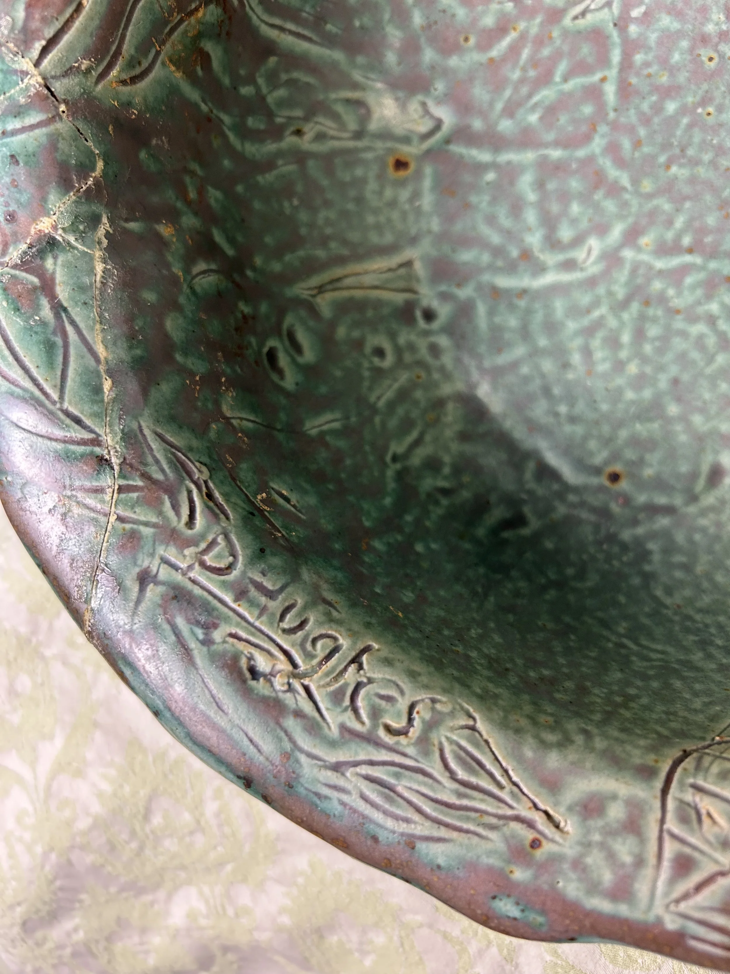 Close-up of a greenish ceramic or metal bowl with the inscription 'PRUETGSK' and some etched leaf designs.