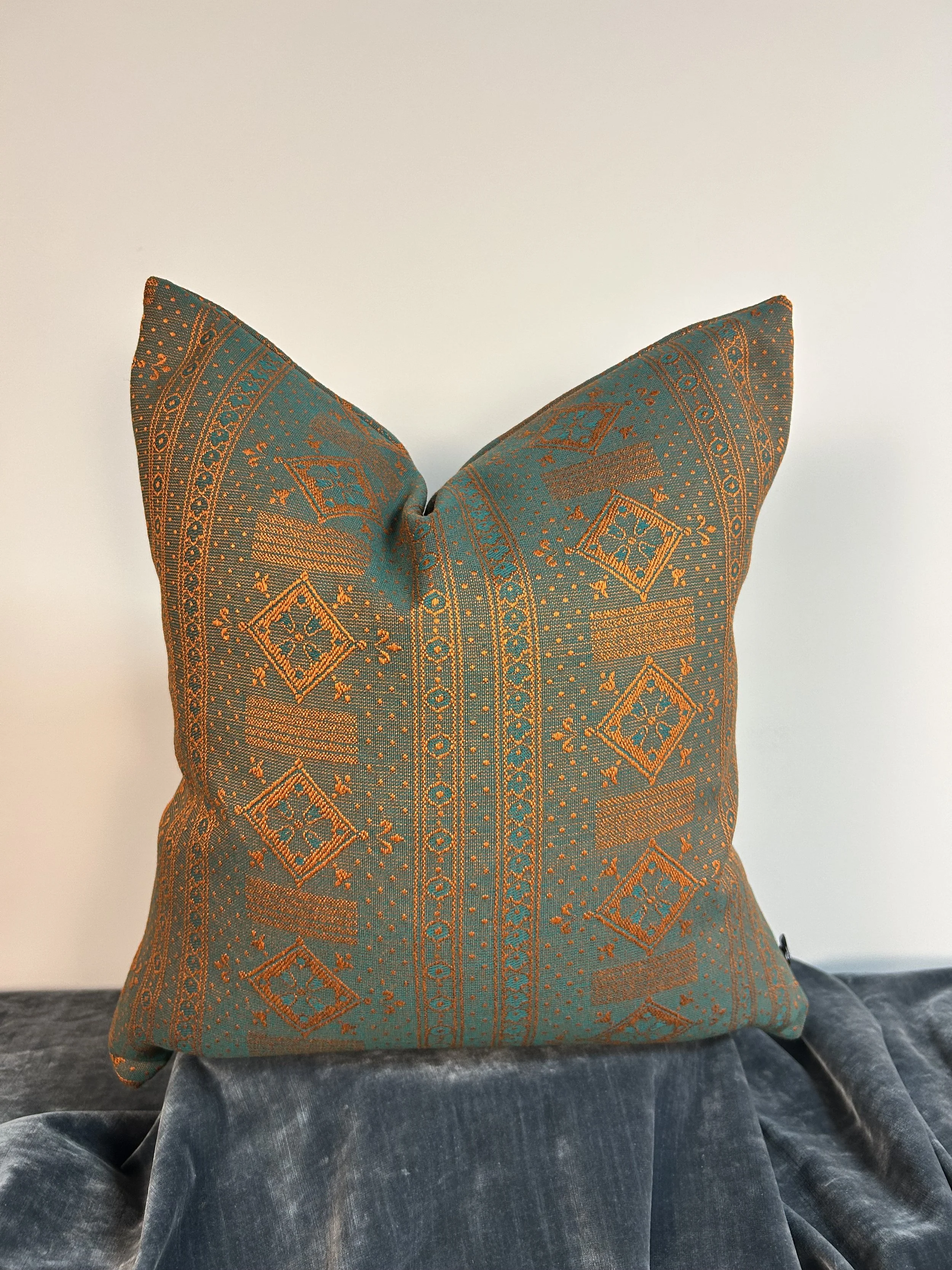 Decorative cushion with intricate blue and gold pattern resting on a blue velvet surface.