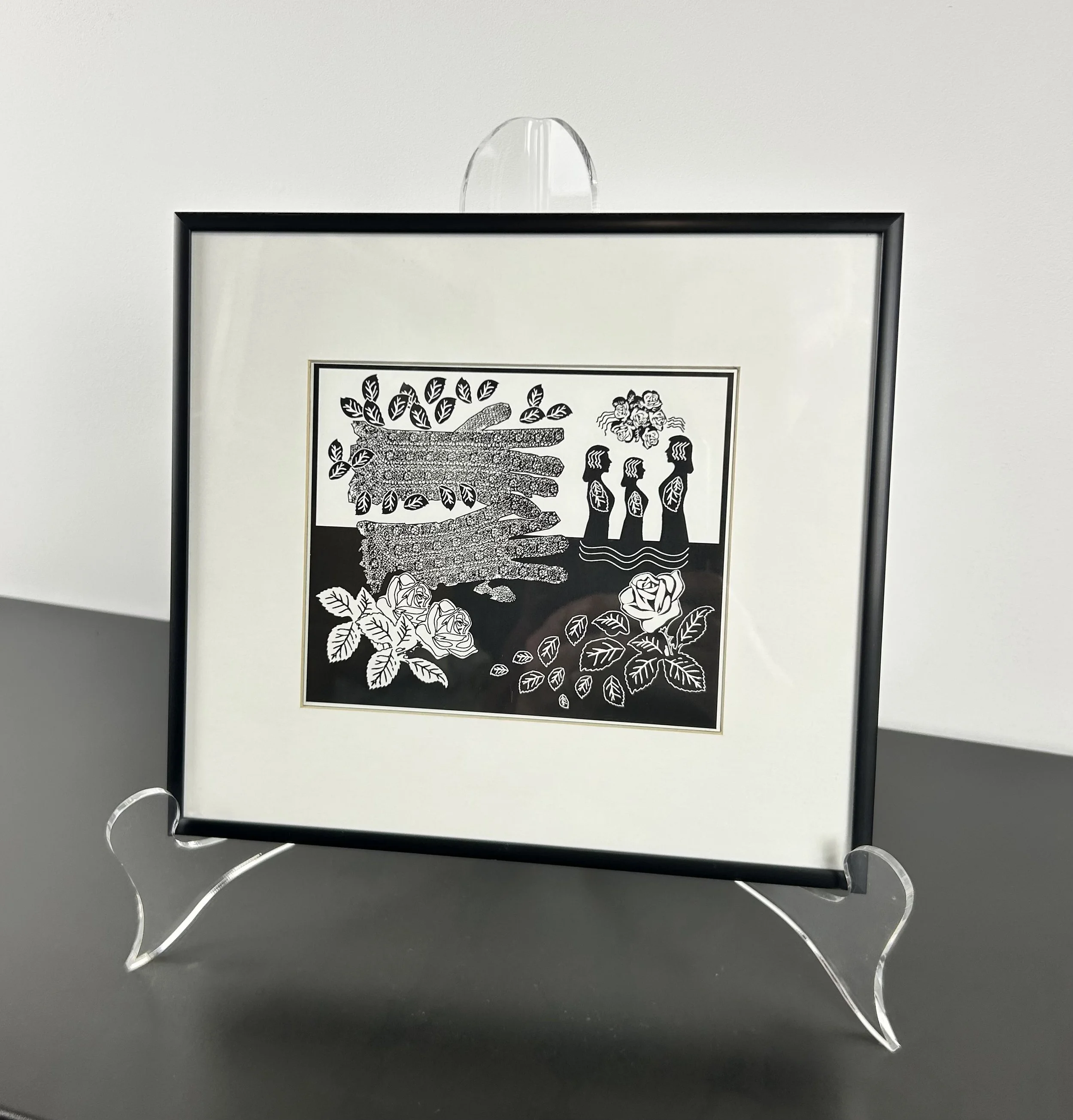 Black and white framed artwork depicting three women with flowers above their heads, a large hand with leaves and flowers, and roses with leaves surrounding the scene.