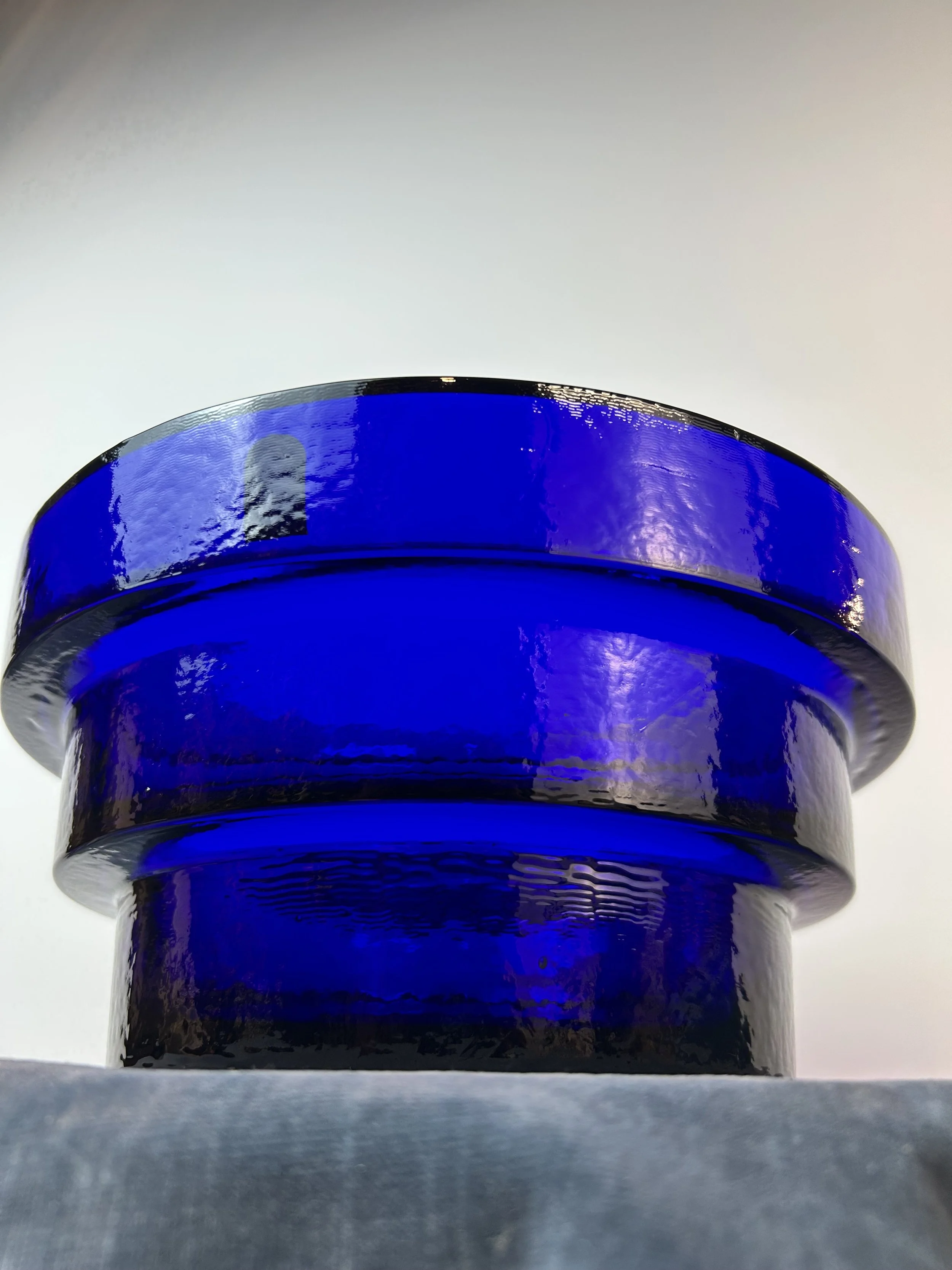 Close-up of a stack of three deep blue glass bowls or plates viewed from below, against a plain light background.