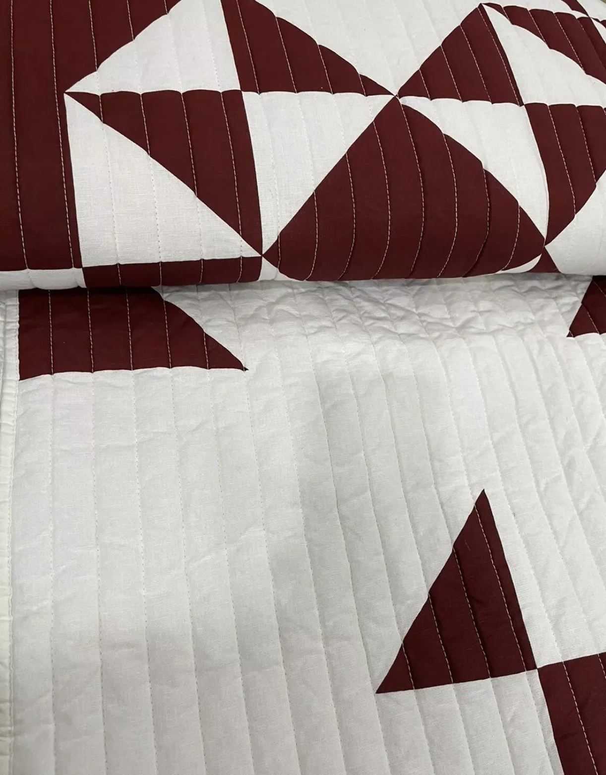 Close-up view of a quilt with a red and white geometric pattern including triangles and stripes.