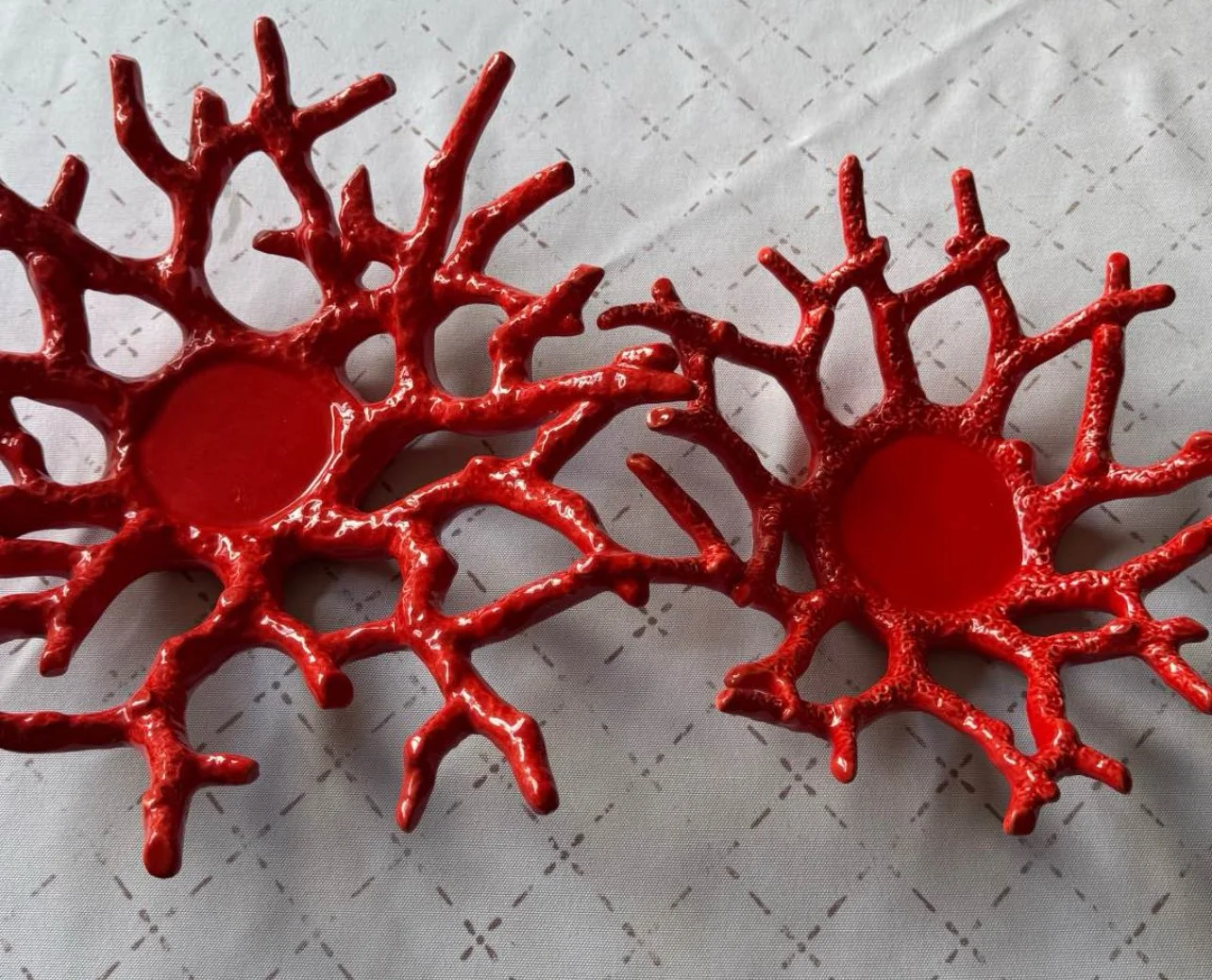 Two red coral-shaped candle holders on a patterned light-colored surface.
