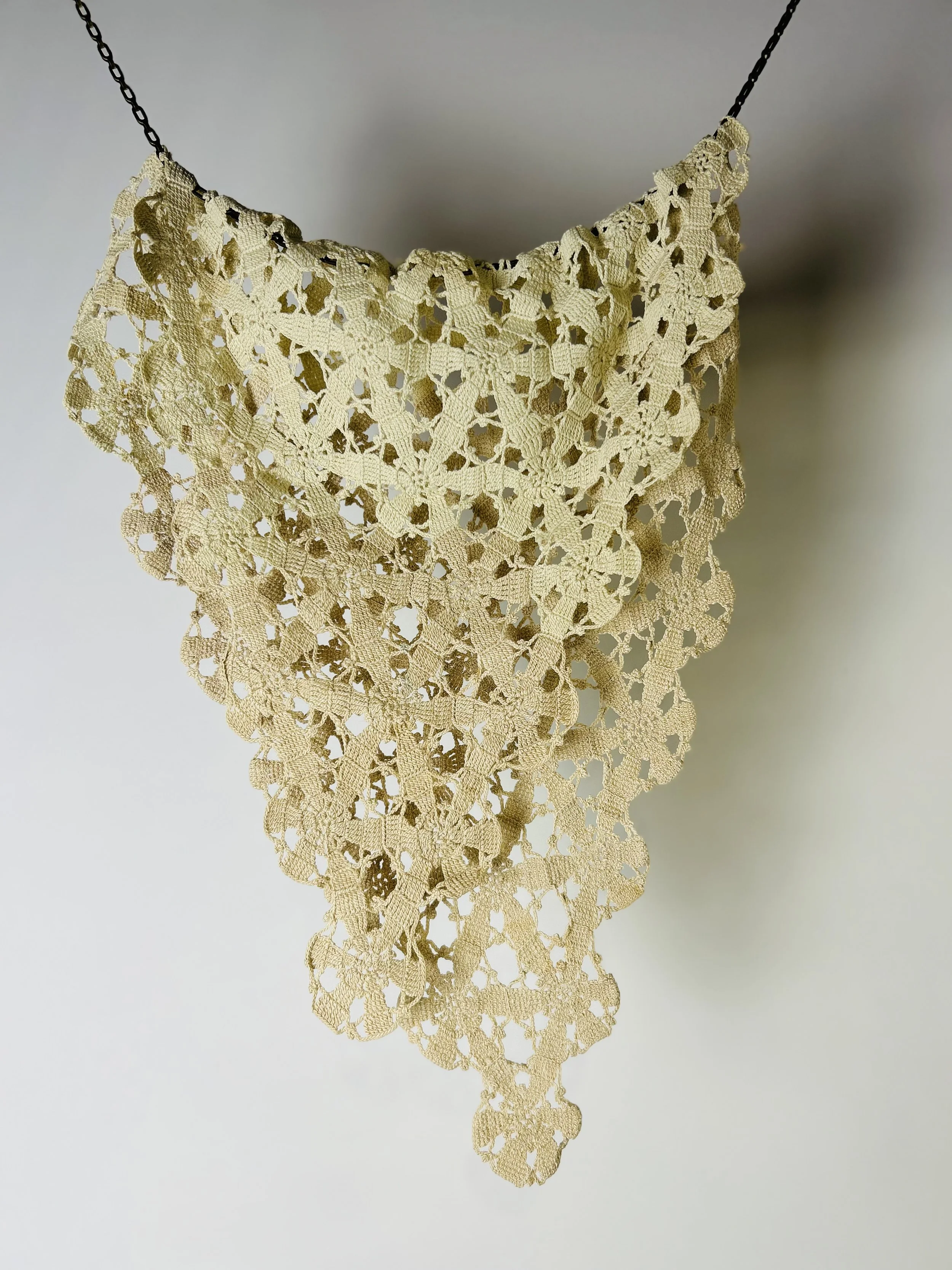 Beige lace crochet collar hanging on a black chain