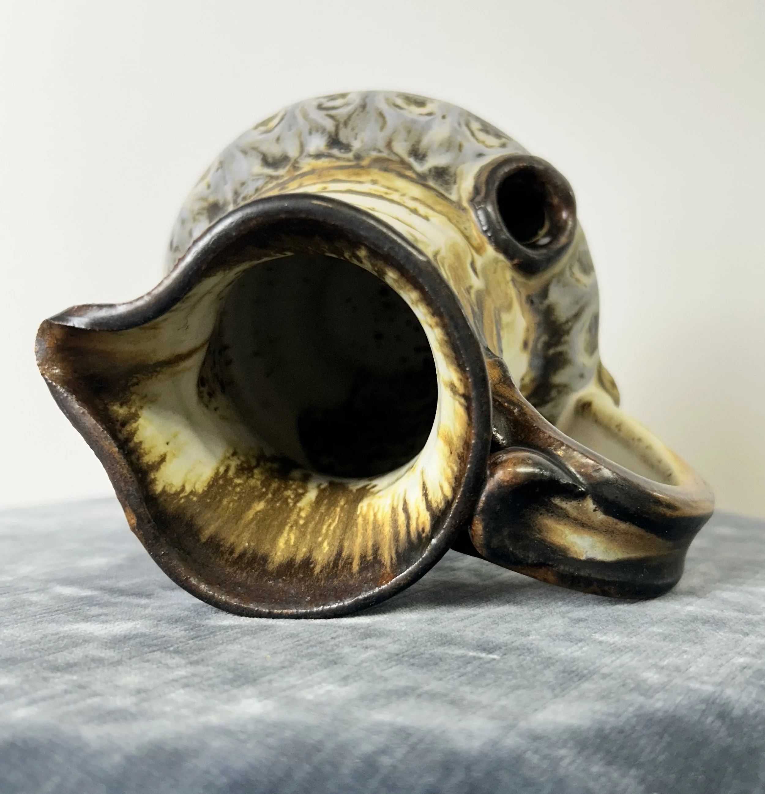 A ceramic teapot with a marbled brown and cream finish, lying on its side on a gray fabric surface.
