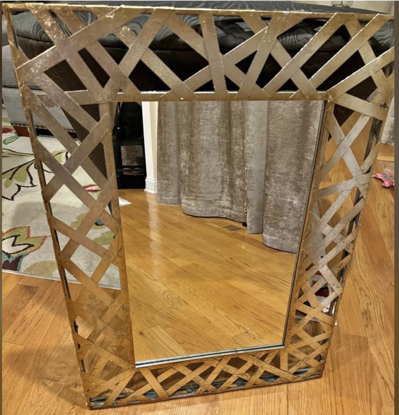 Decorative square mirror with a wooden lattice frame on a hardwood floor in a living room.