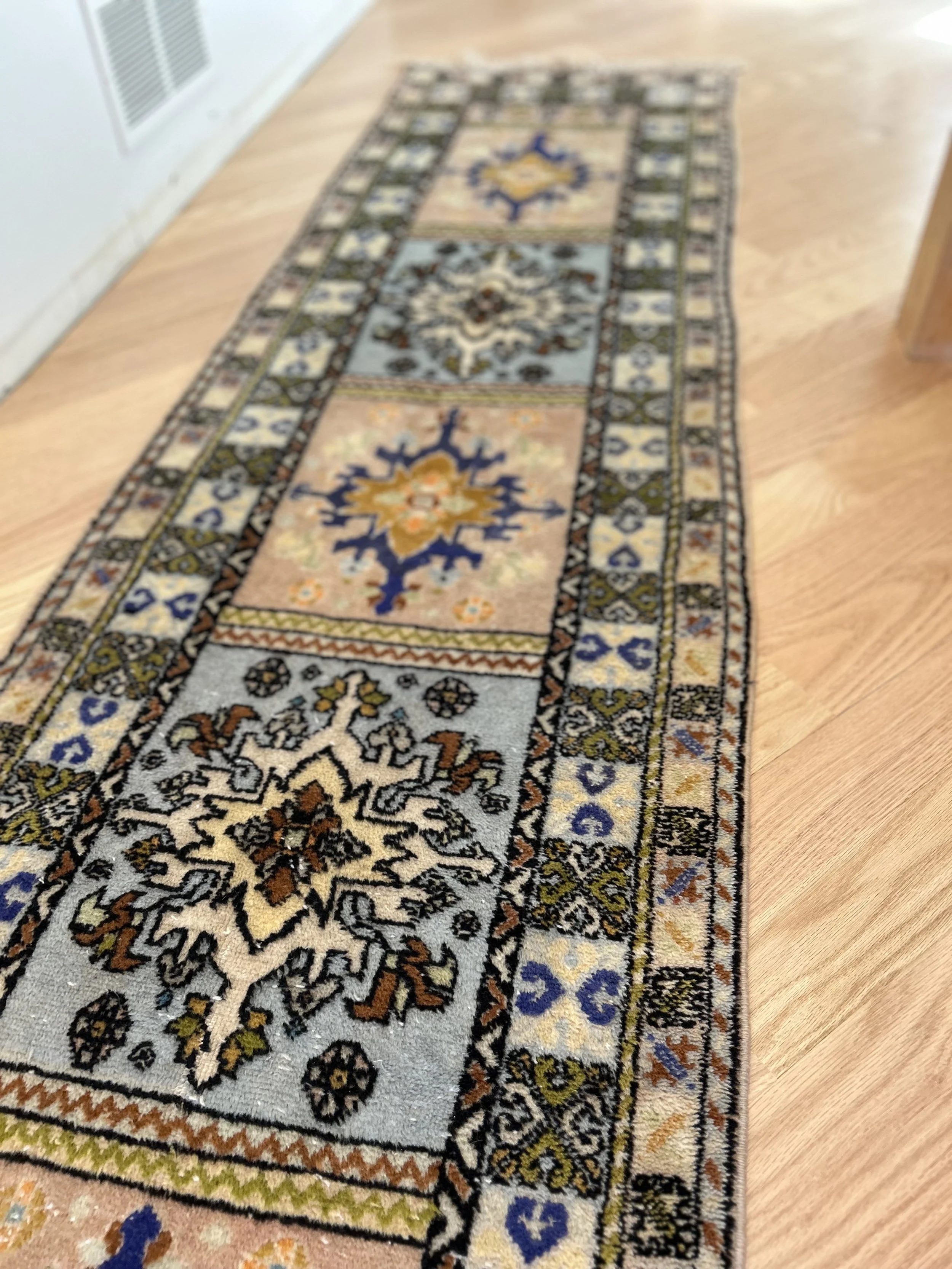 A long, rectangular area rug with intricate patterns and a variety of colors including blue, beige, rust, and black, placed on a wooden floor.