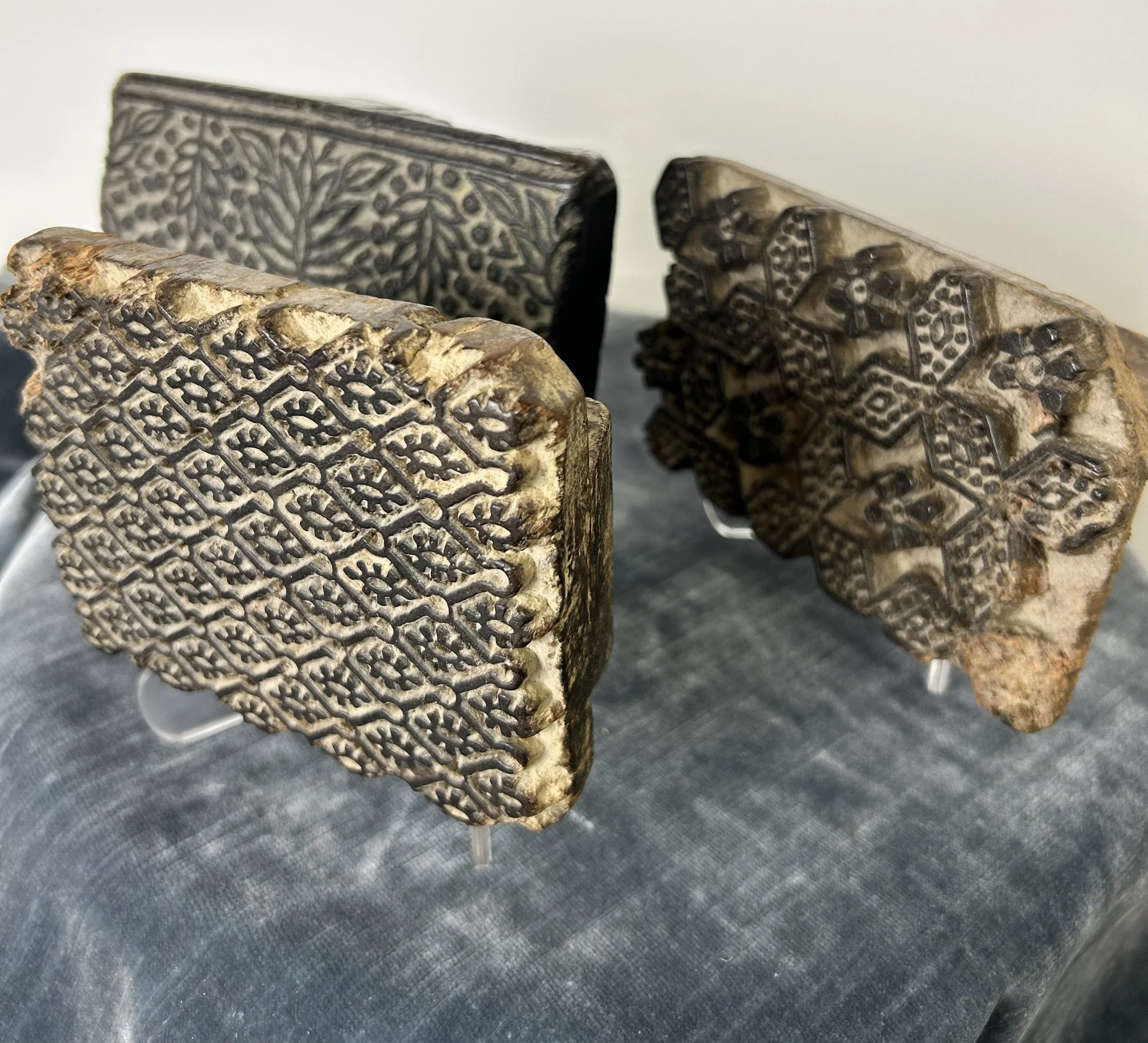 Three carved wooden blocks with intricate geometric and floral patterns displayed on stands.