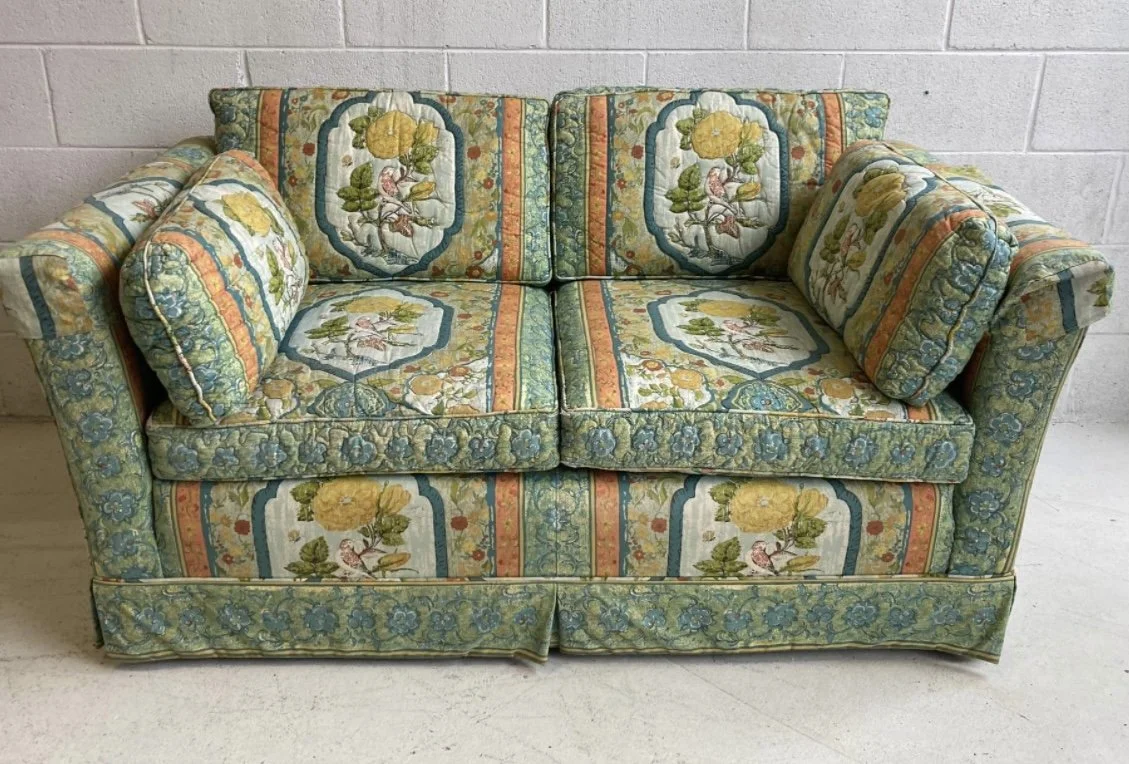 A vintage fabric sofa with floral and striped pattern, featuring matching cushions, placed against a plain wall.