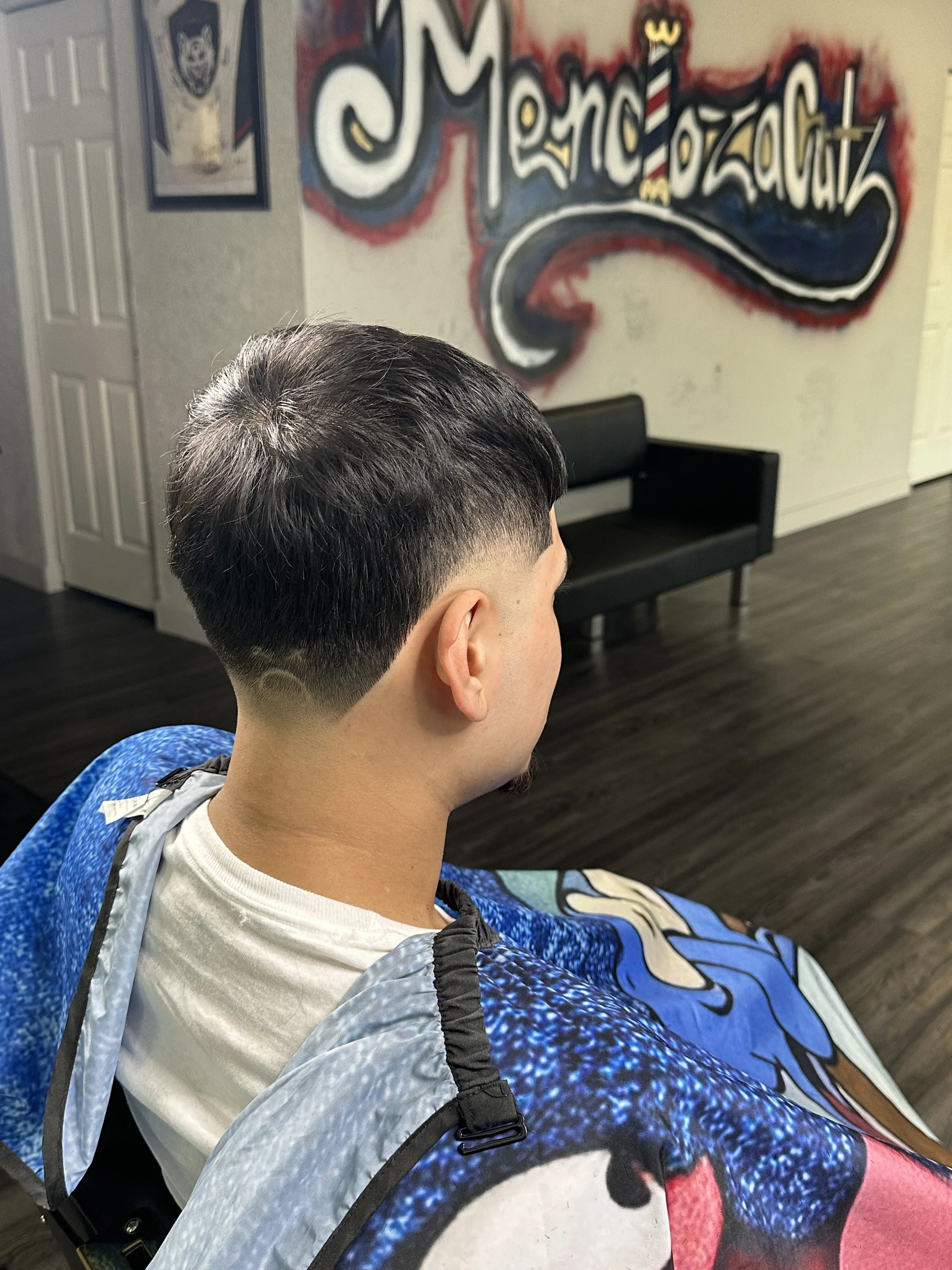 A man with a freshly styled haircut sitting in a barber's chair. The background features a wall with graffiti-style artwork and text reading 'Mondo Mozzato'.