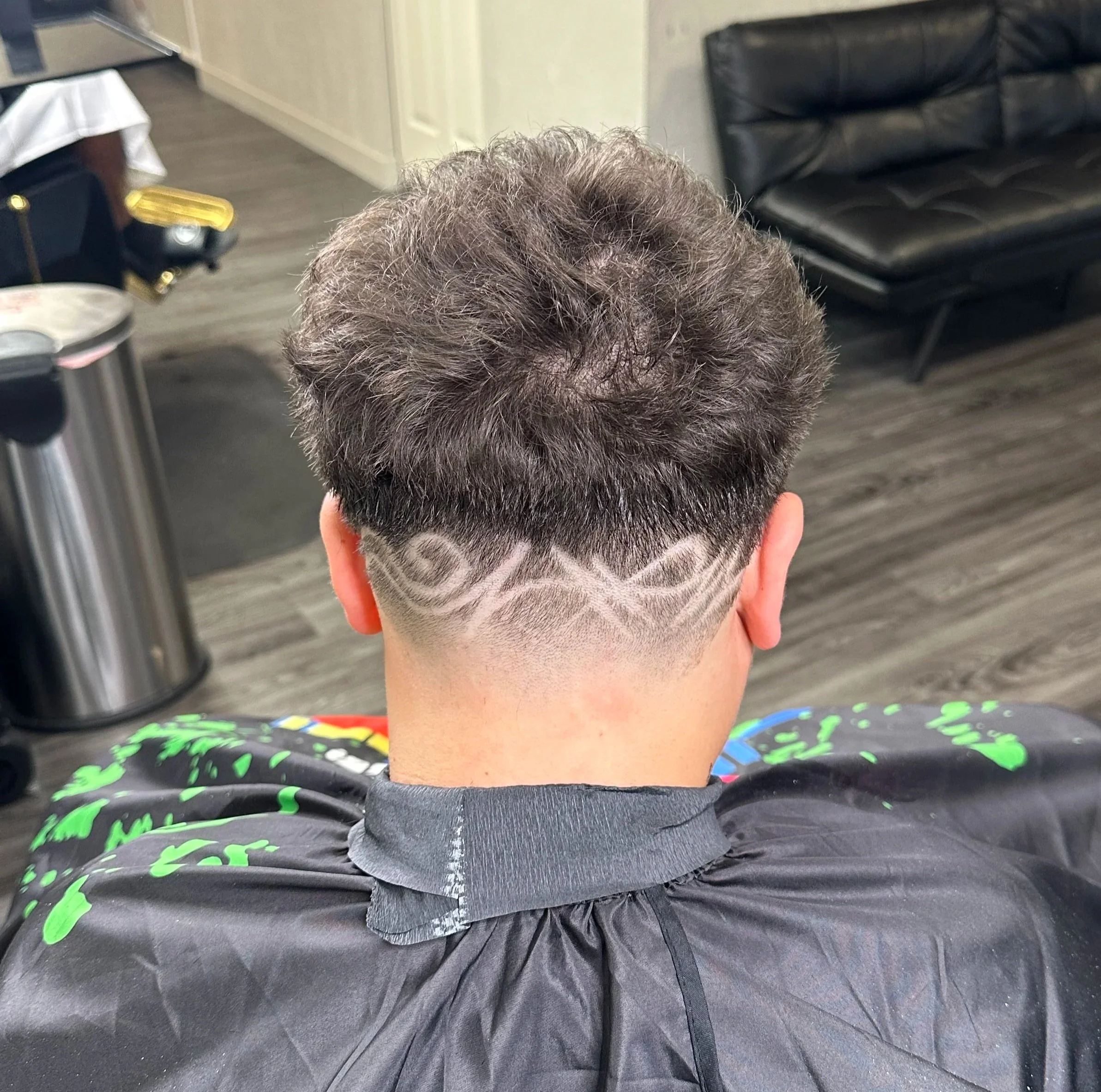 Back of a man's head with a fresh haircut featuring a tattoo-like design shaved into the hair below the crown.