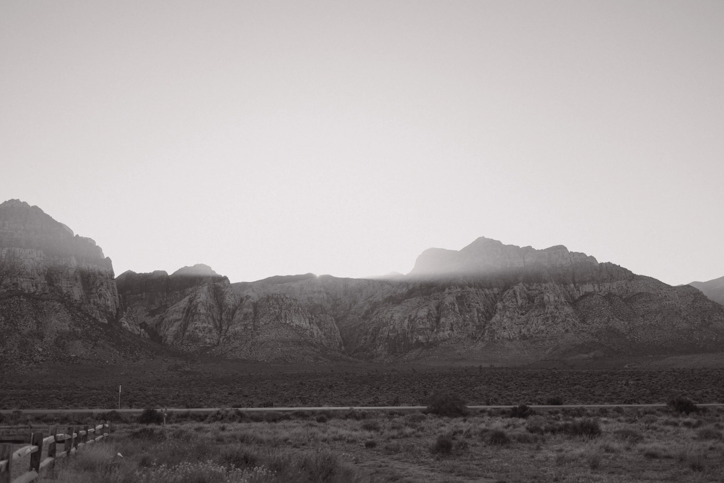 Black and white landscape of mountain range with a flat foreground and minimal vegetation.