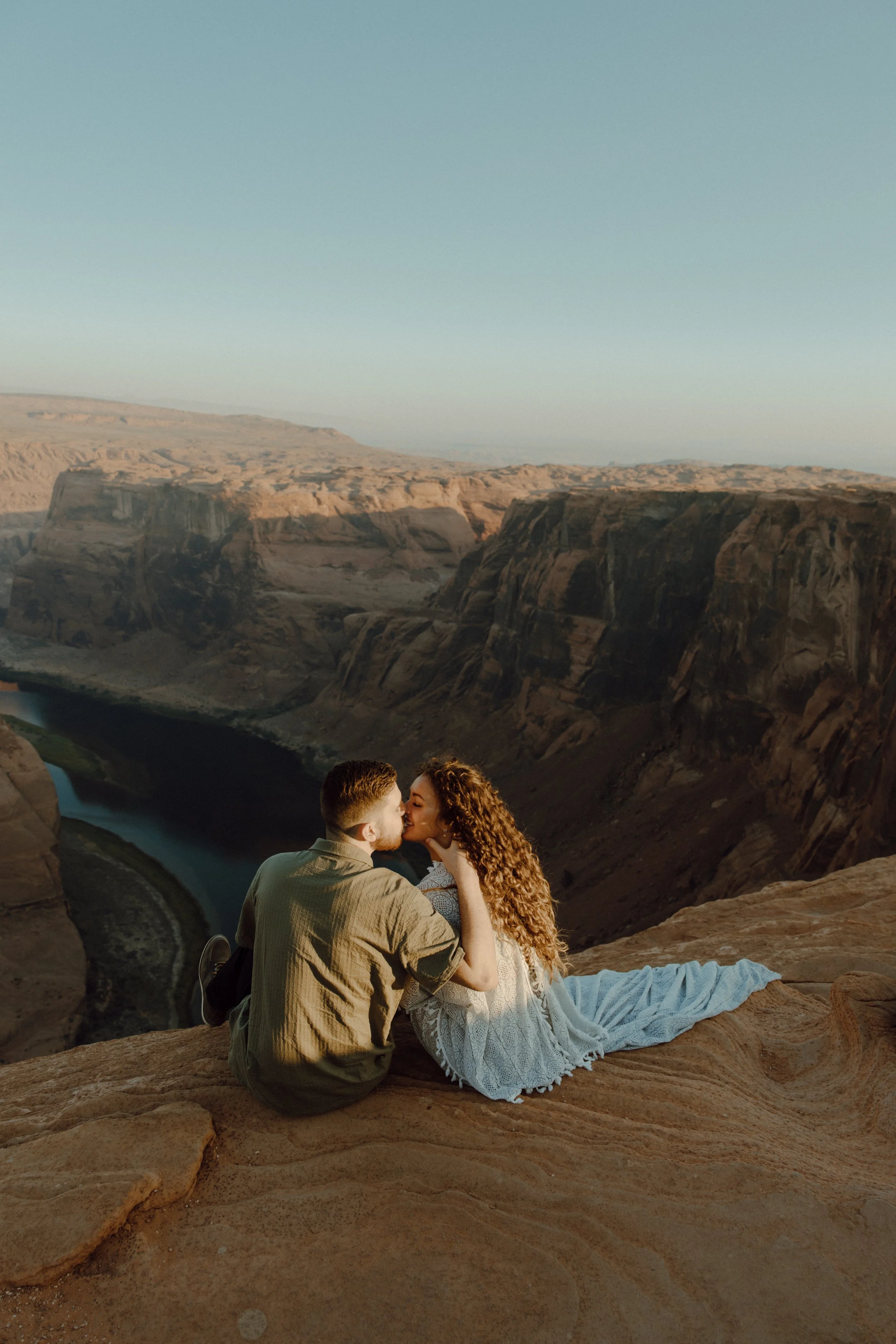 A couple sharing a kiss on a rocky overlook at Horseshoe Bend during sunrise