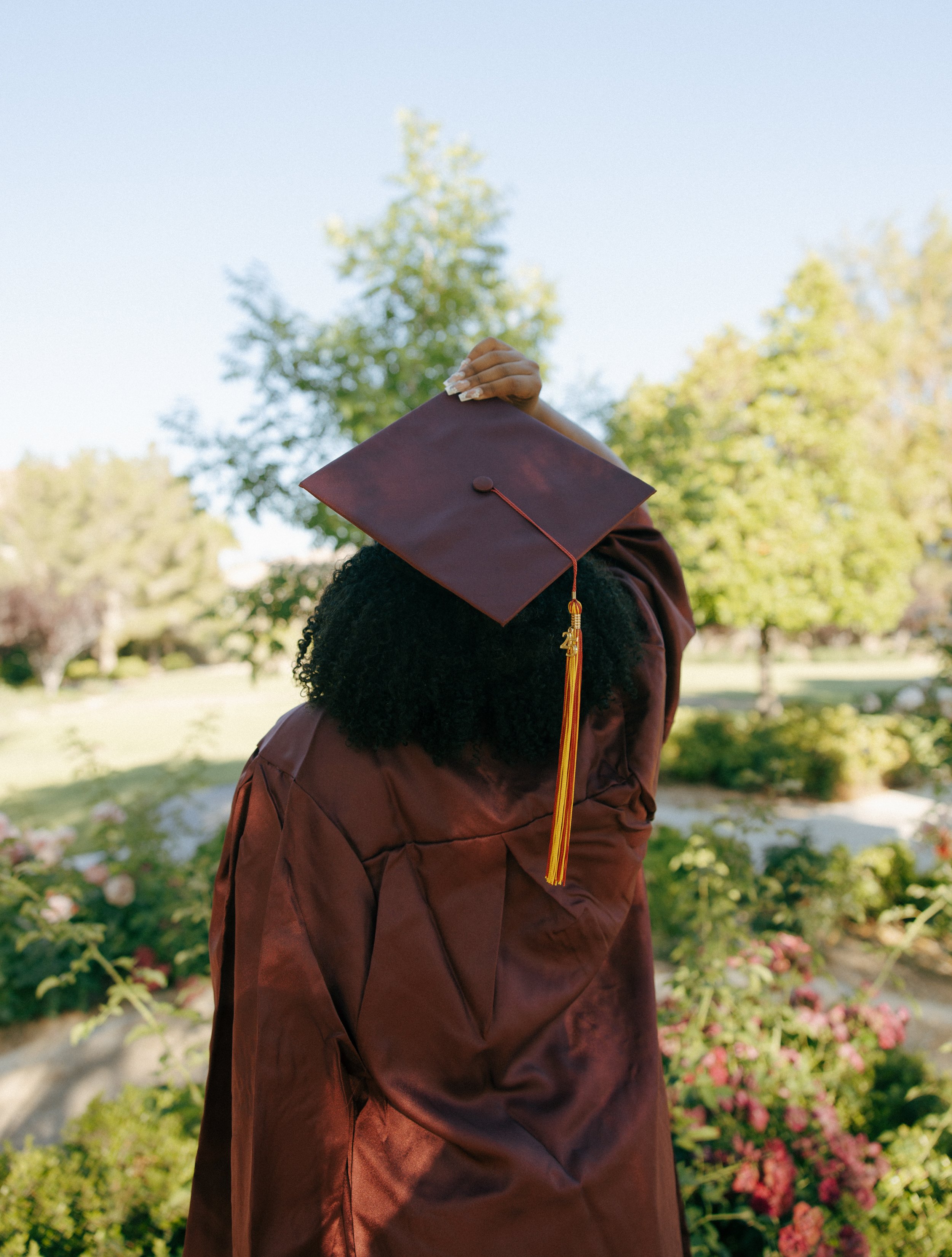 Graduation cap and gown outdoors with trees and bushes in the background.