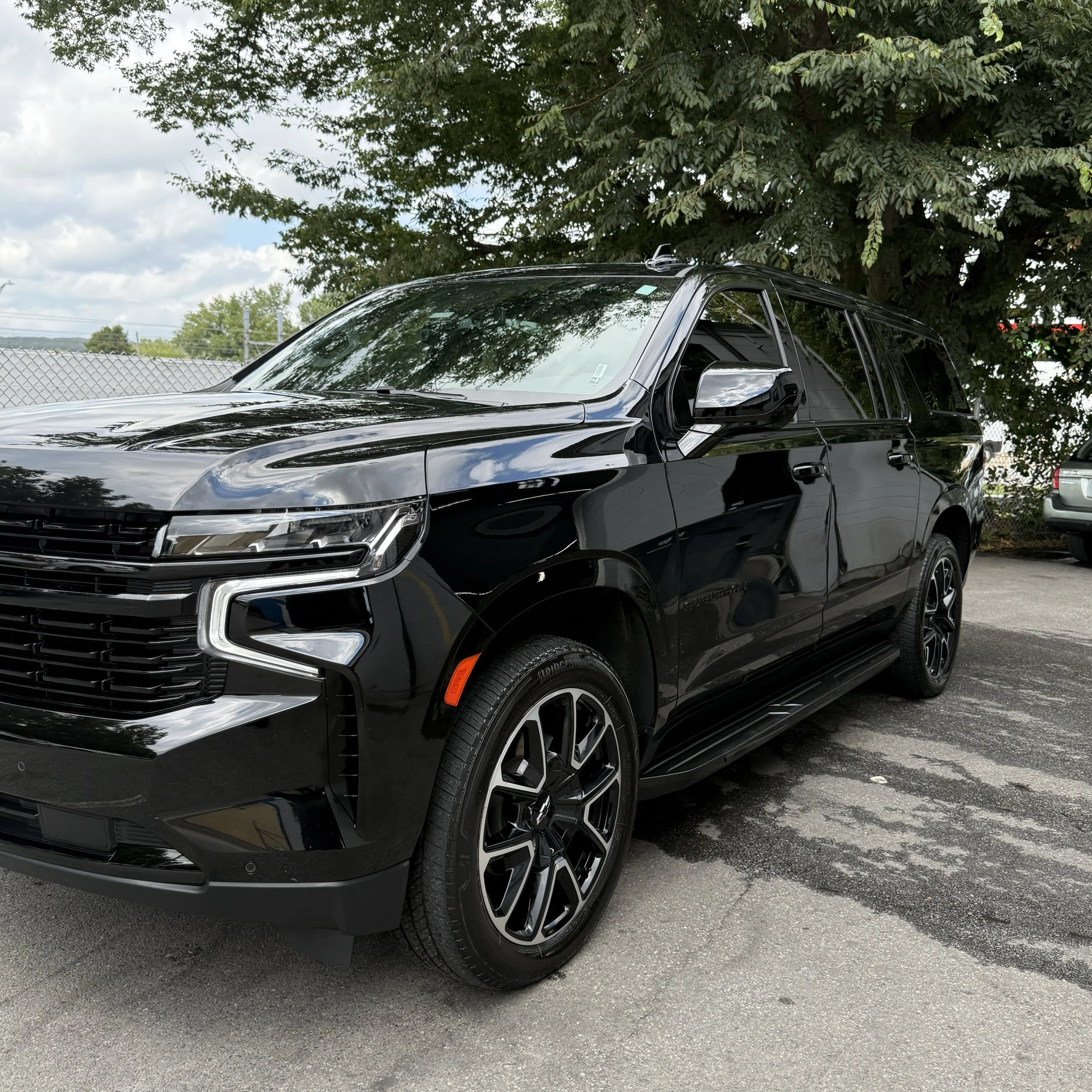 Black SUV parked on a paved lot with trees in the background.