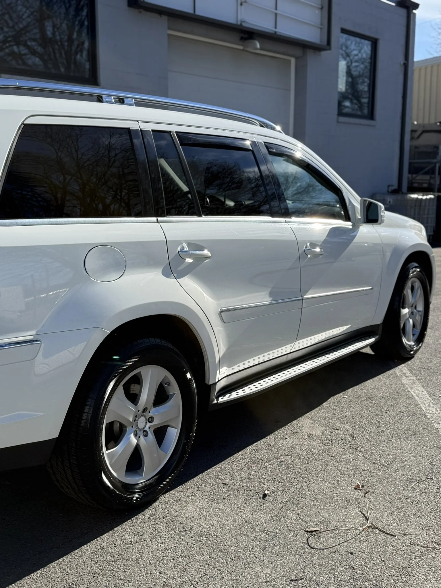 A white SUV parked outside a modern building with large windows and a garage door in daylight.