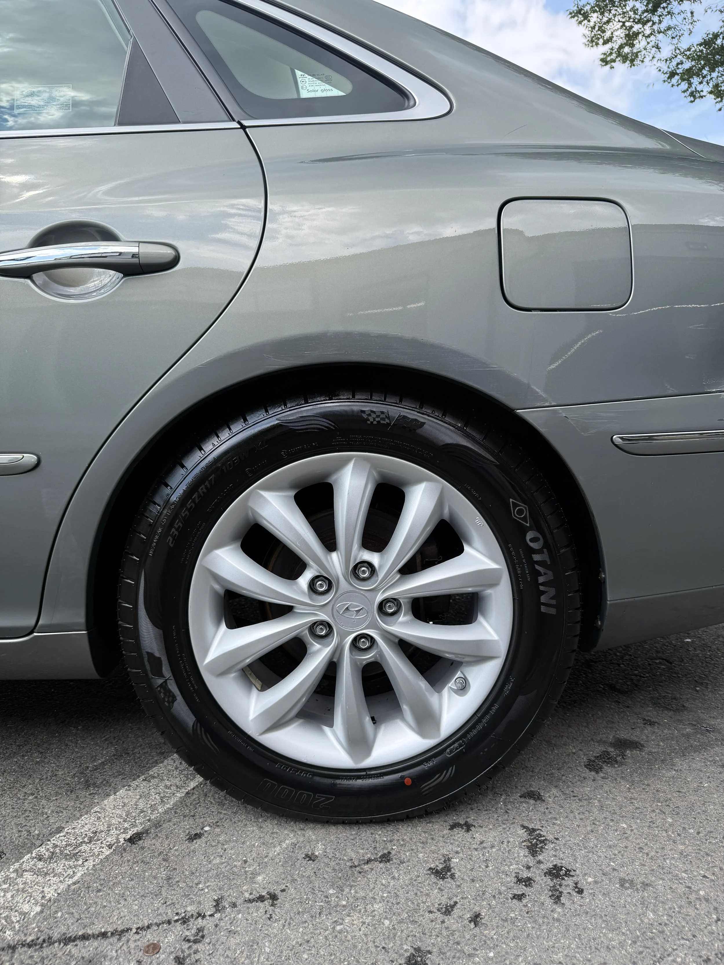 Close-up of a silver Hyundai car's rear quarter panel and wheel, parked on asphalt with a parking line visible.