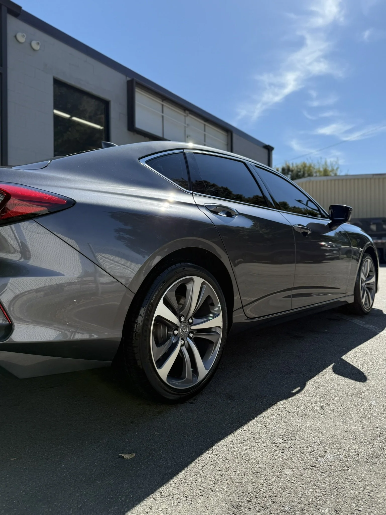 A silver sedan car parked outdoors on a sunny day, with a building and a clear blue sky in the background.