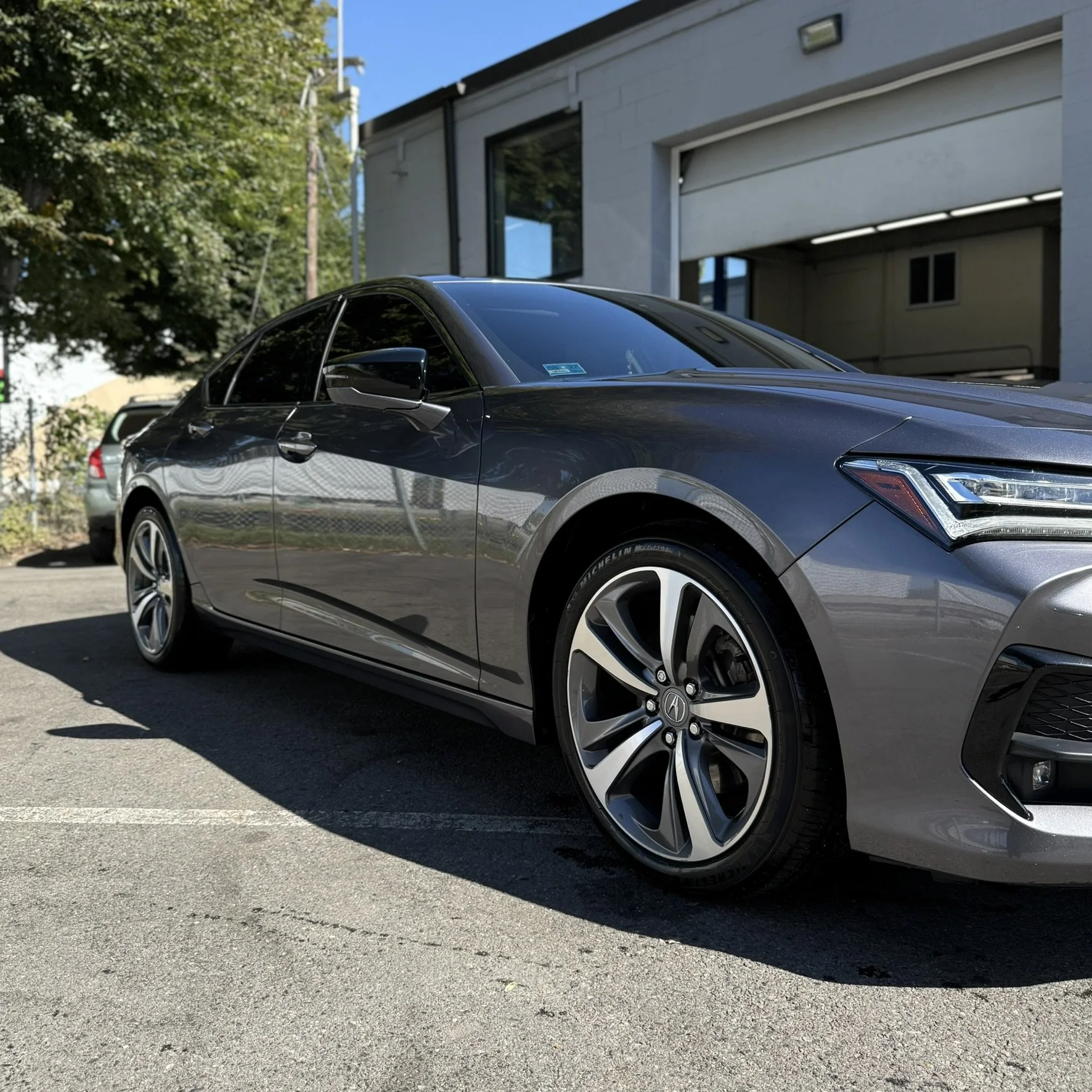 A grey luxury sedan parked on an outdoor parking lot under a clear blue sky.